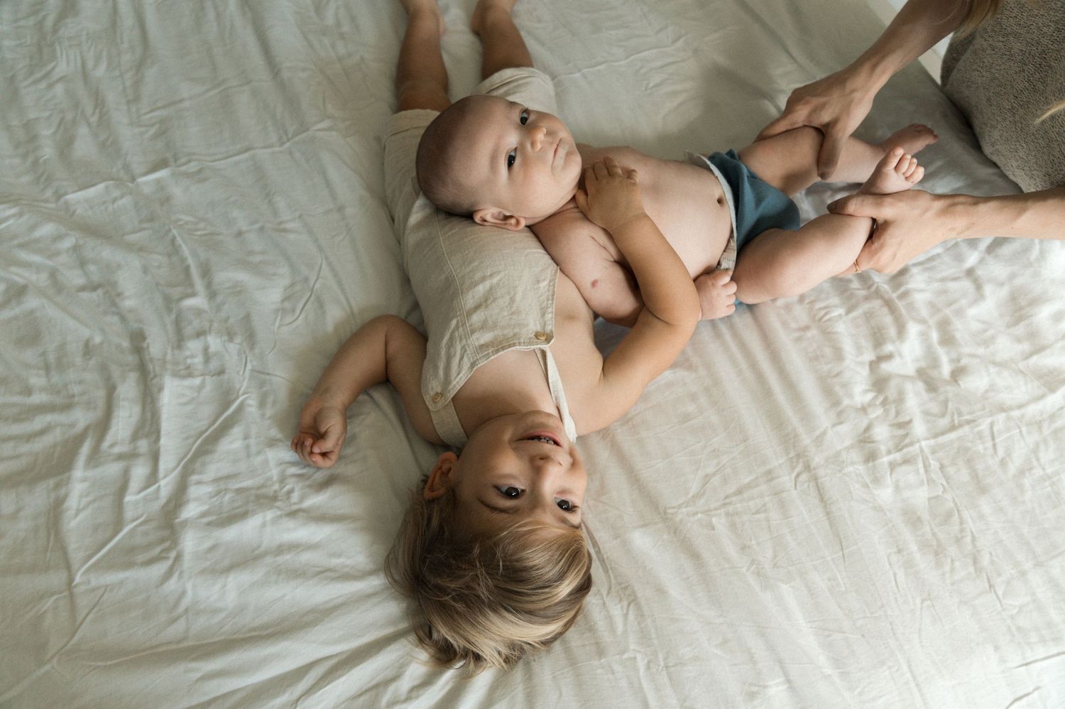 A baby lies on white bedding while rolling and playing in different positions.