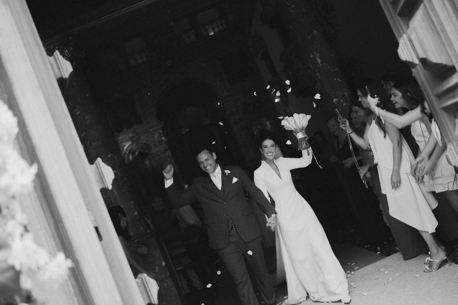 Black and white photo of a bride and groom exiting their wedding ceremony as guests celebrate around them.