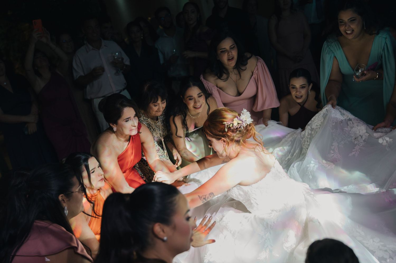 Wedding guests dance underneath a voluminous white dress on the dance floor during a celebration.