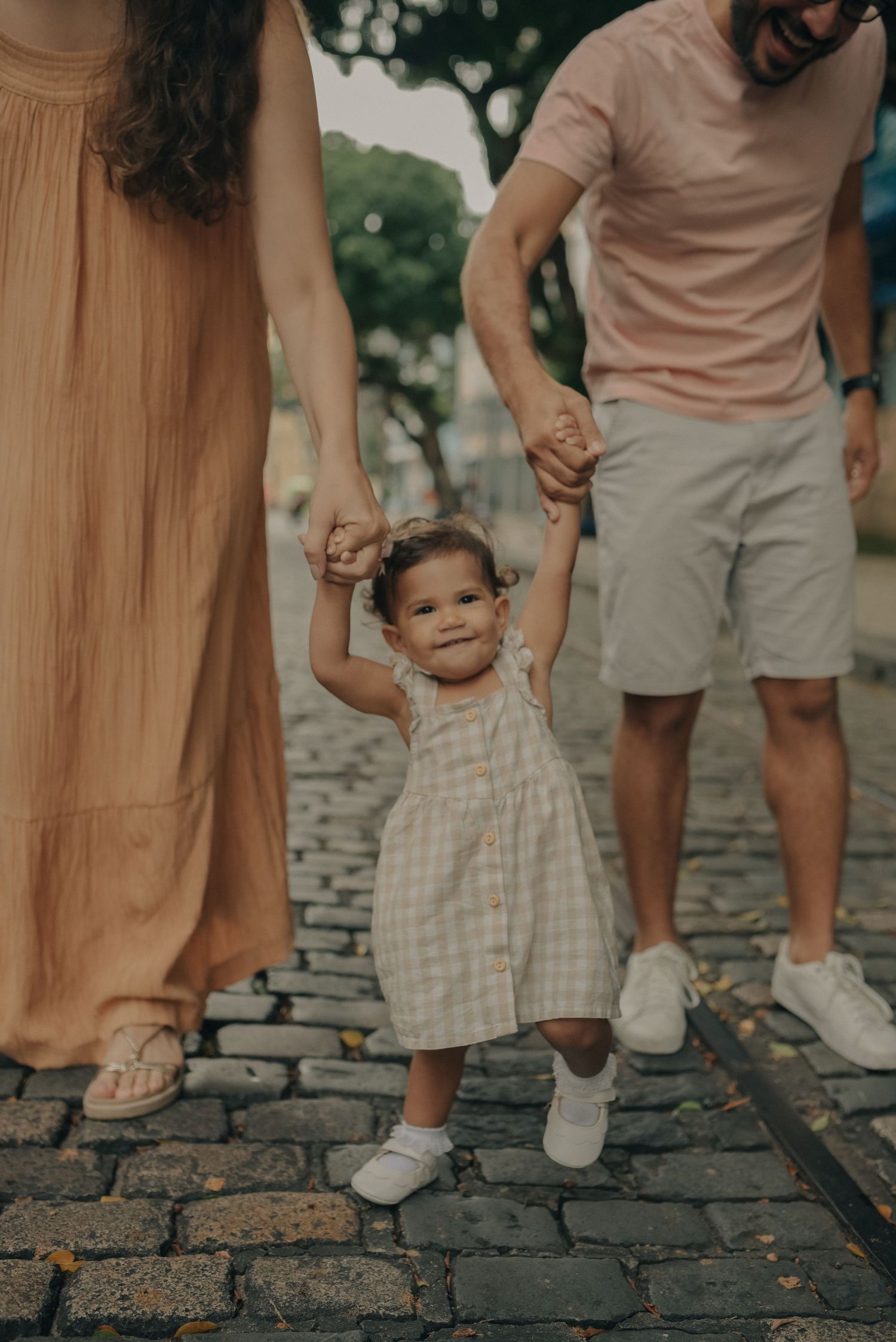 Small child walking on cobblestones while holding hands with parents.