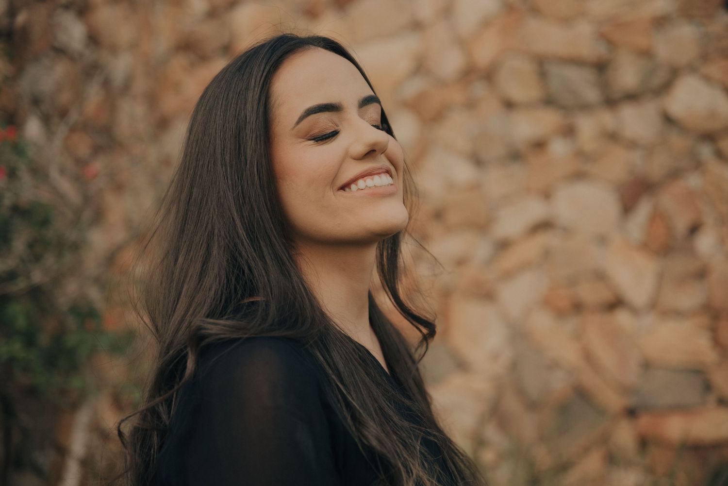 Portrait of someone smiling with closed eyes against textured stone wall background.