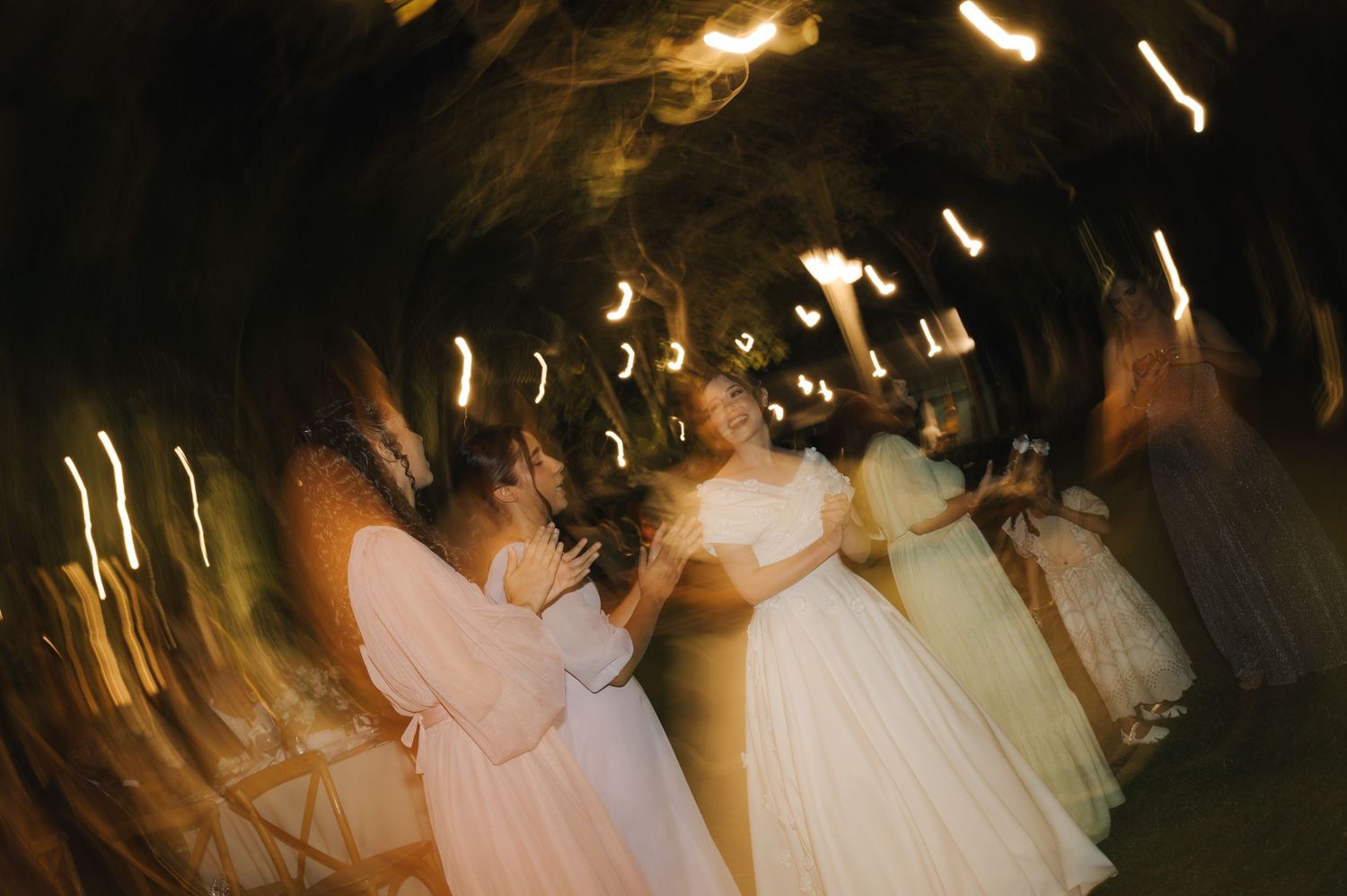 A dreamy motion-blur capture of wedding guests dancing in pink and white dresses.