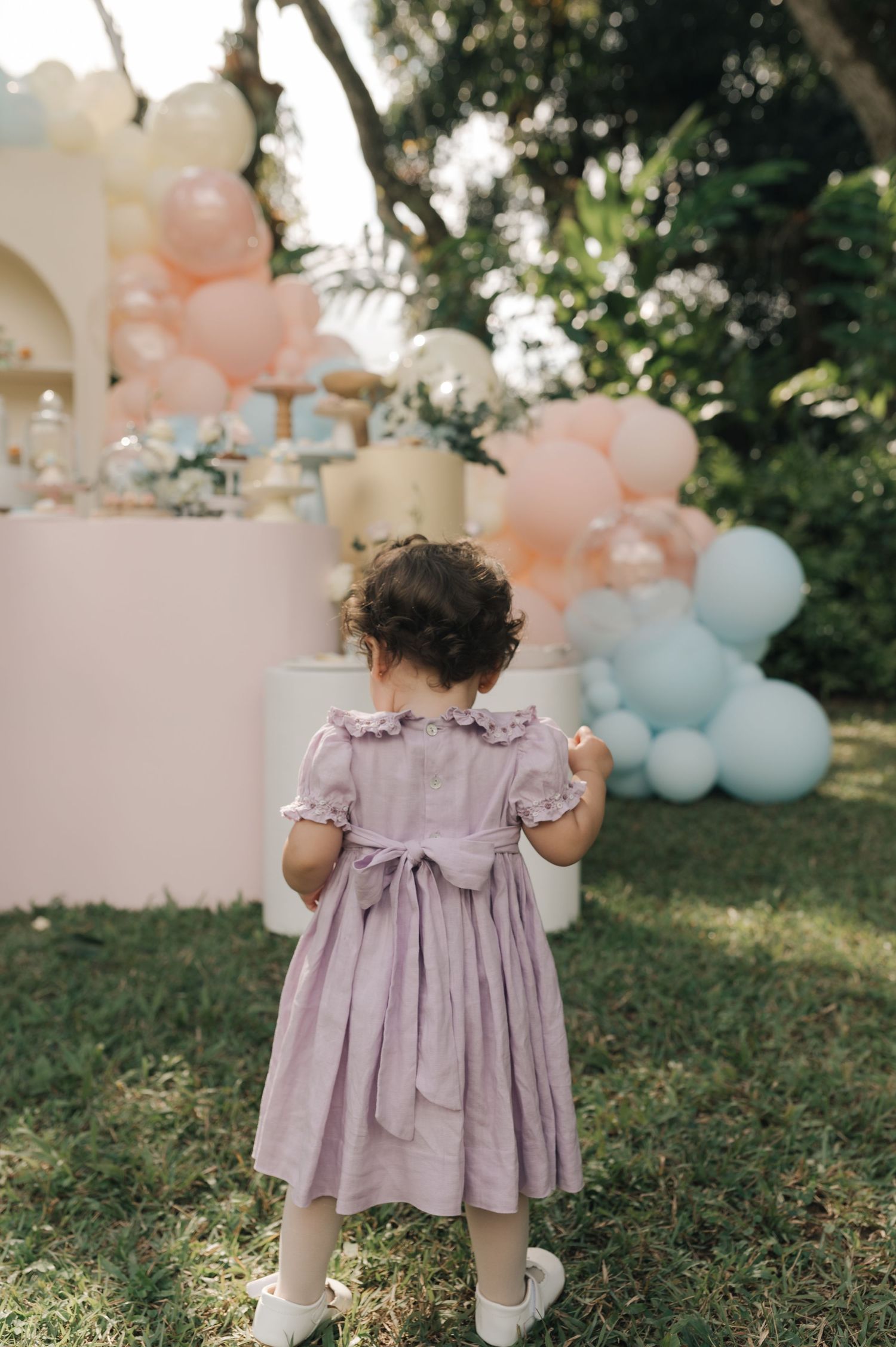 Child in purple dress standing near party decorations with pastel balloons.