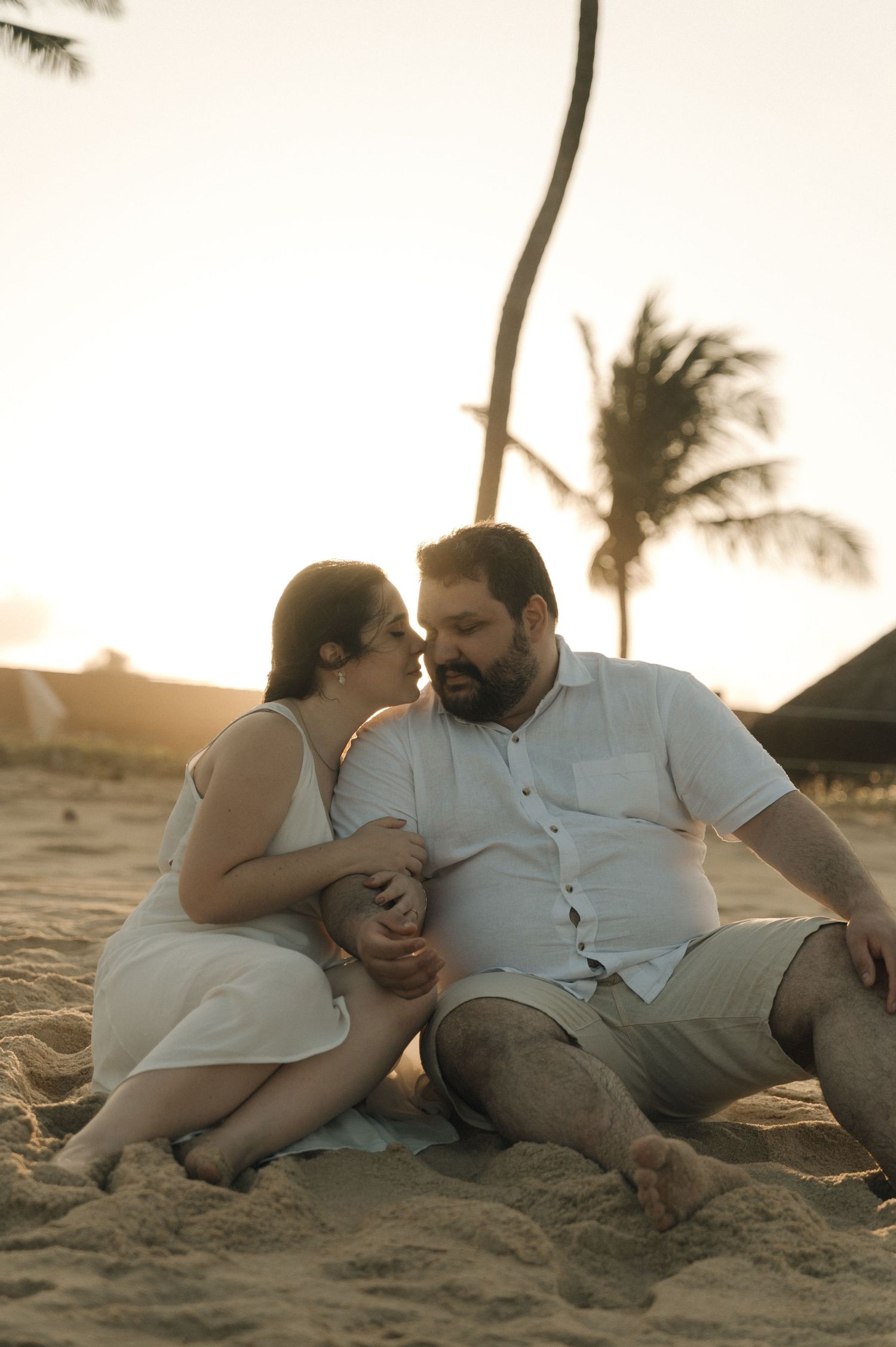 A couple sharing an intimate moment while sitting on sandy beach at sunset.
