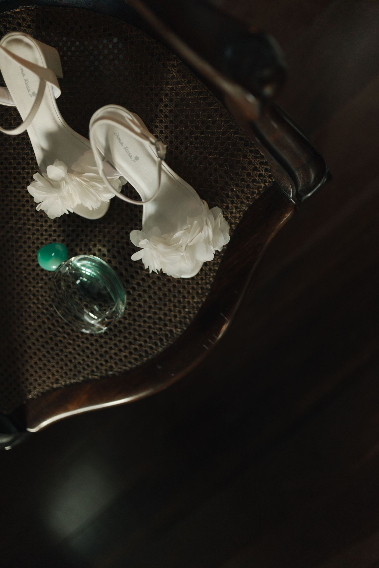 Elegant white bridal shoes and perfume bottle on a textured dark surface.