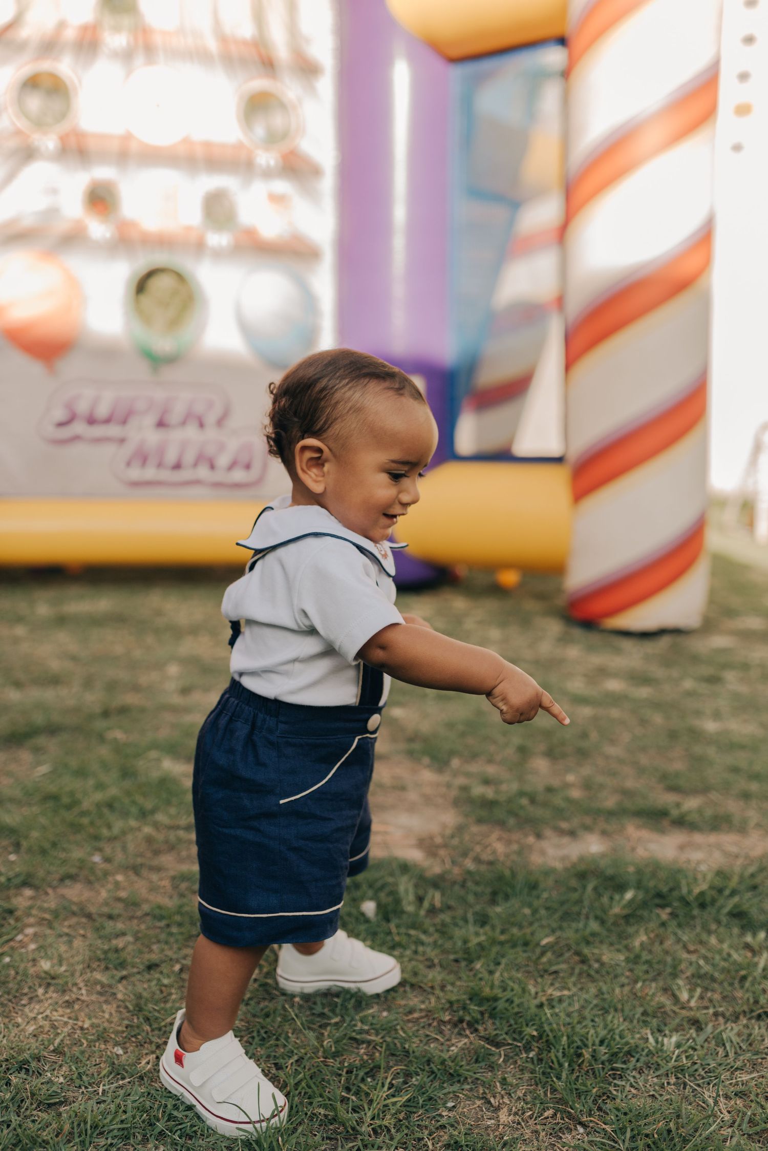 Toddler in suspenders playing near inflatable bounce house with striped patterns.