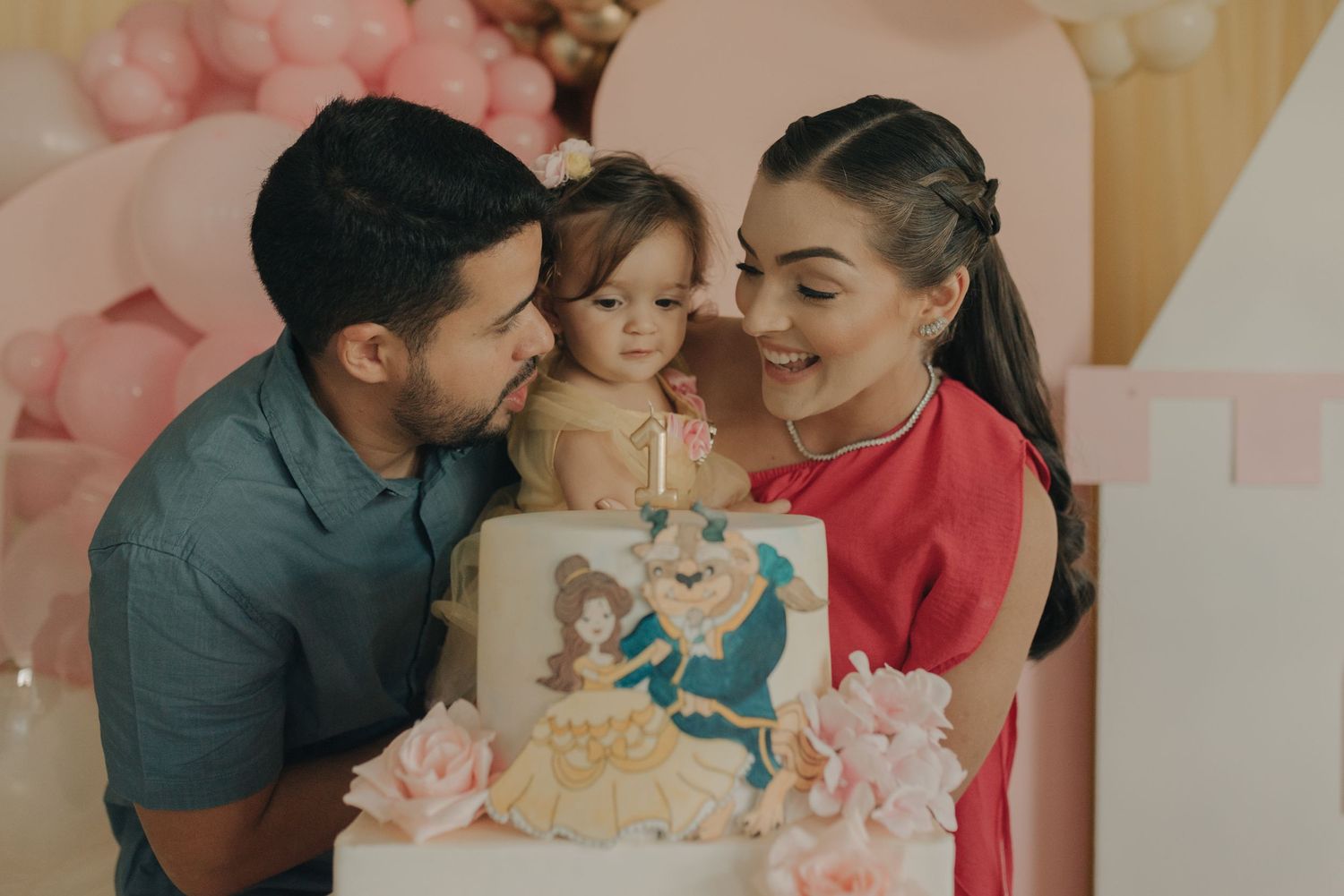 A celebration scene with a decorated cake and pink balloon arch in the background.