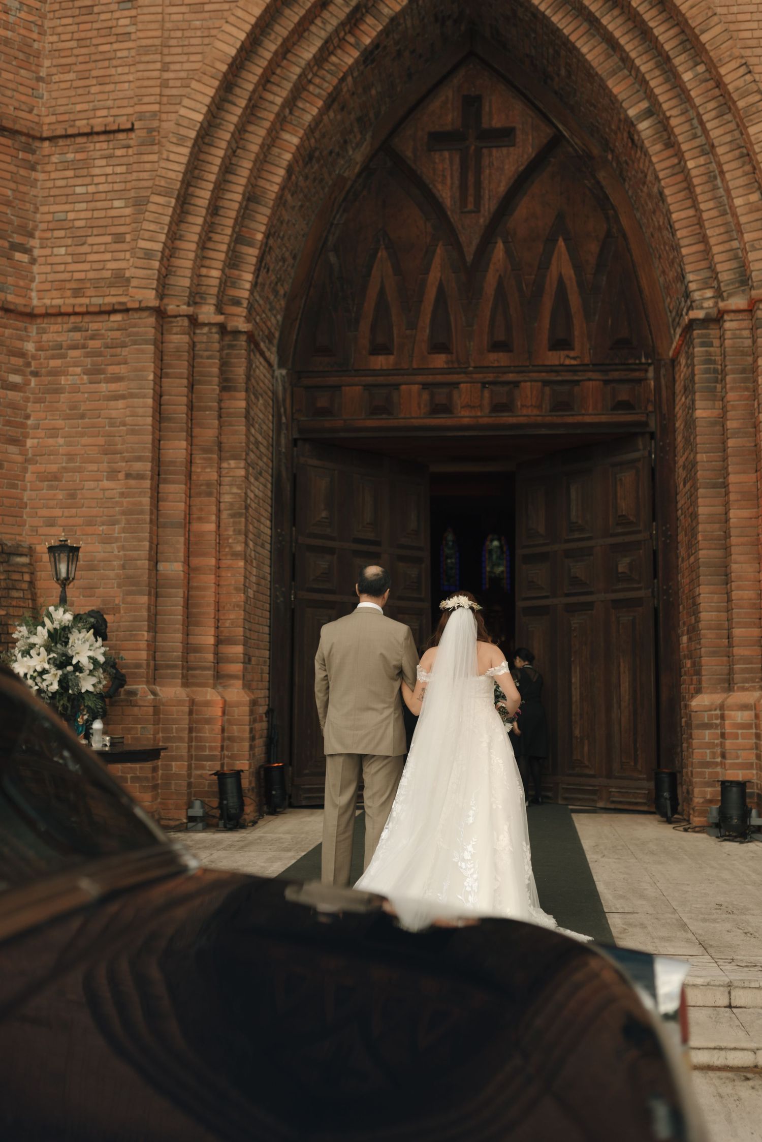 A couple stands at the entrance of a brick church with Gothic arched doorway during their wedding ceremony.