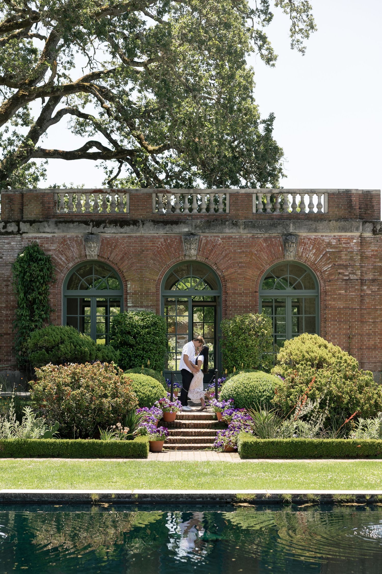 Elegant garden venue with brick archways, manicured landscaping and a reflective pool creating a serene outdoor setting.