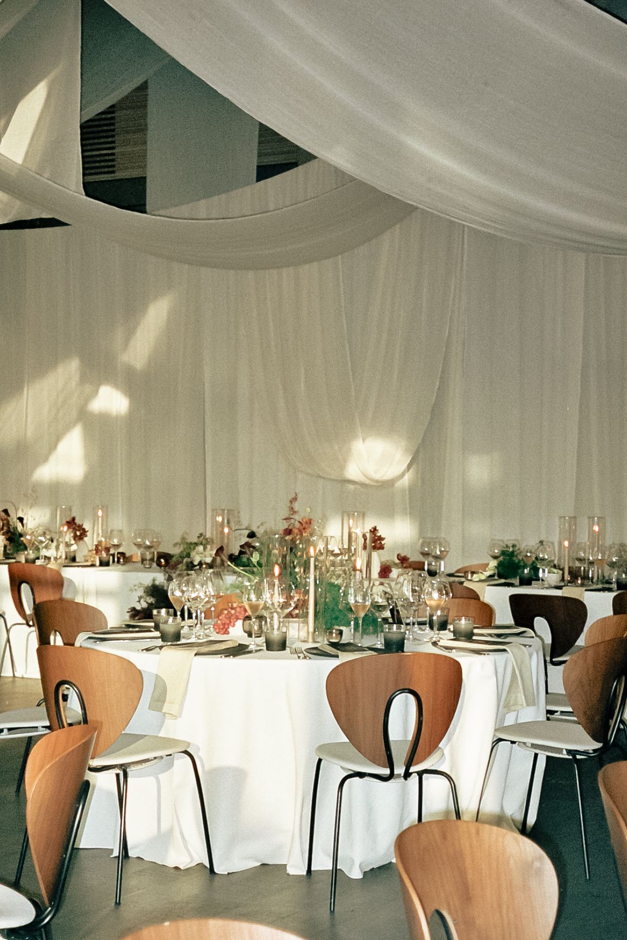 Elegant reception space with white draping, modern brown chairs, and formal table settings.