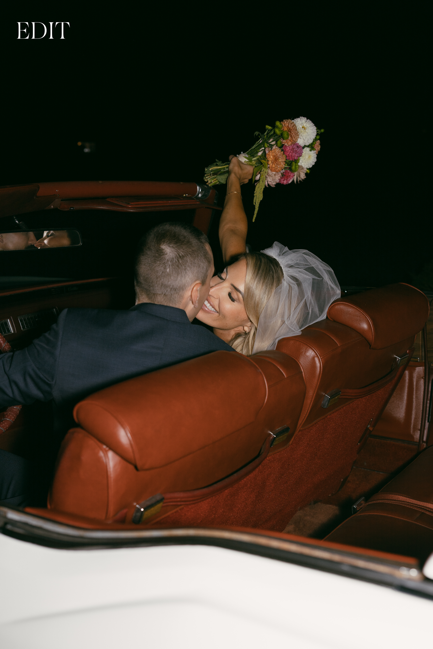 Artistic dark photo of newlyweds in a classic car with red interior.