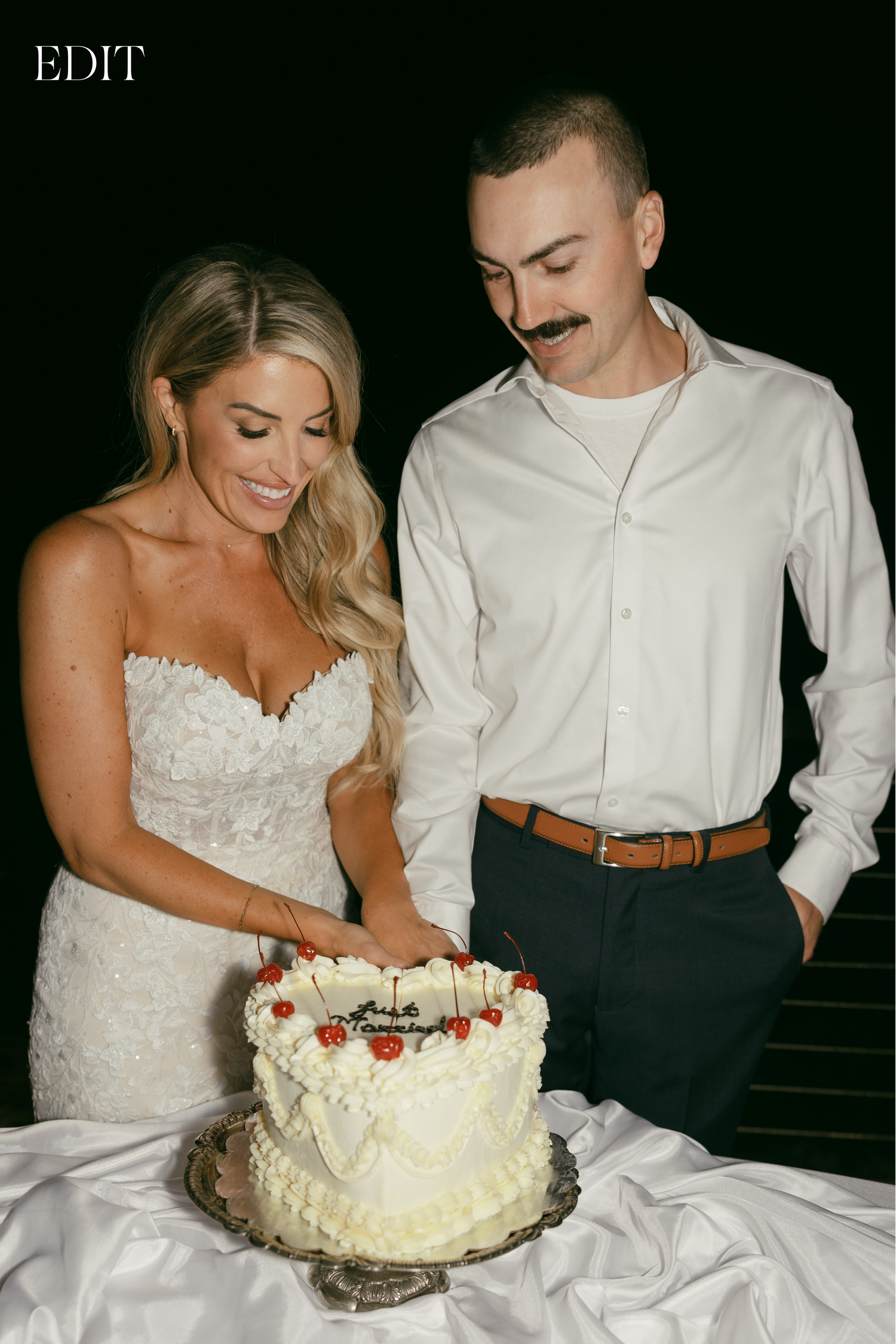 Newlyweds cutting their white wedding cake decorated with strawberries.