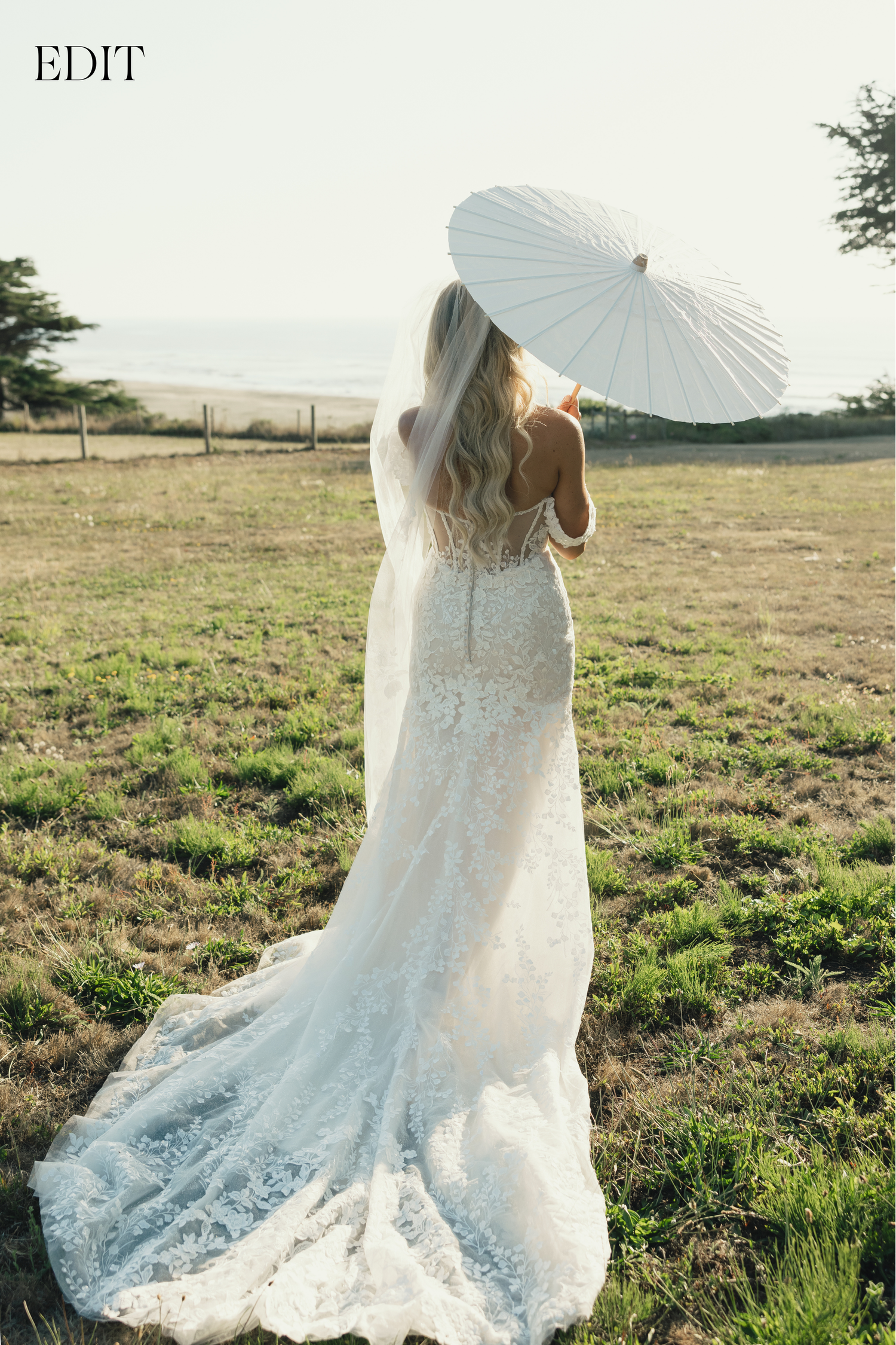 A flowing white lace wedding dress photographed in golden sunlight with a parasol.