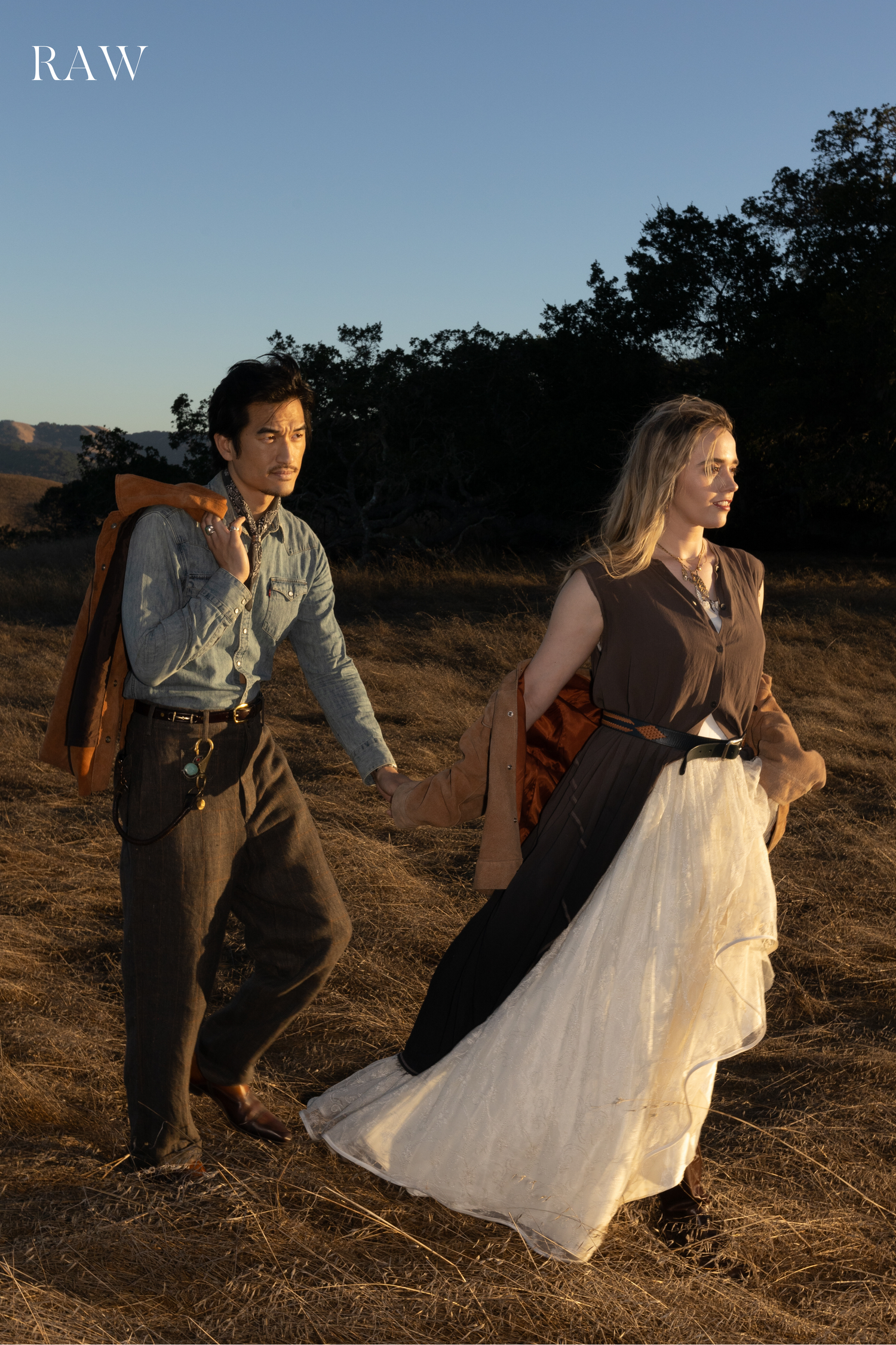 Couple in period clothing run through a rustic field at golden hour.