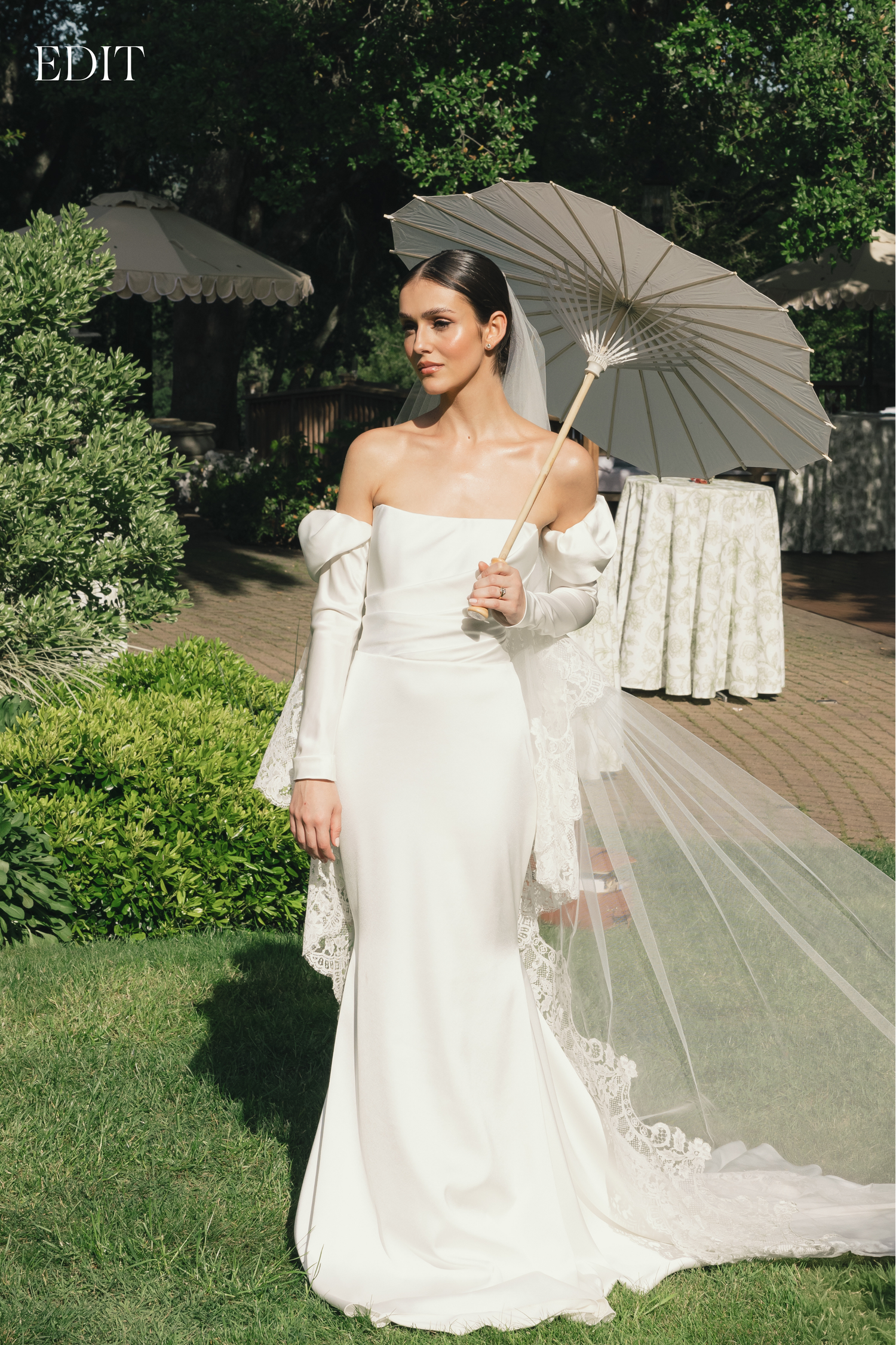 An elegant bride poses with a vintage parasol in a garden setting.
