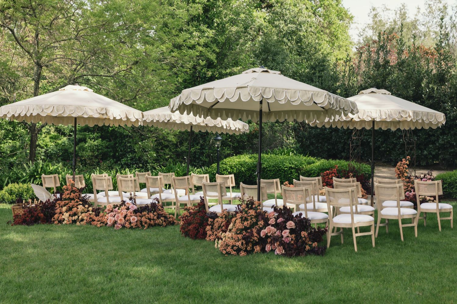 Elegant outdoor wedding ceremony setup with white parasols and chairs on a green lawn.