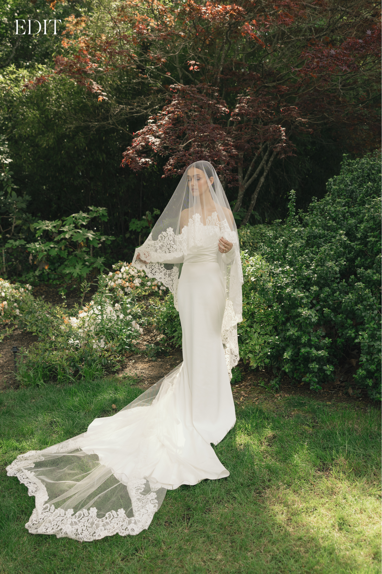 A delicate lace wedding veil flows in the breeze against a garden backdrop.