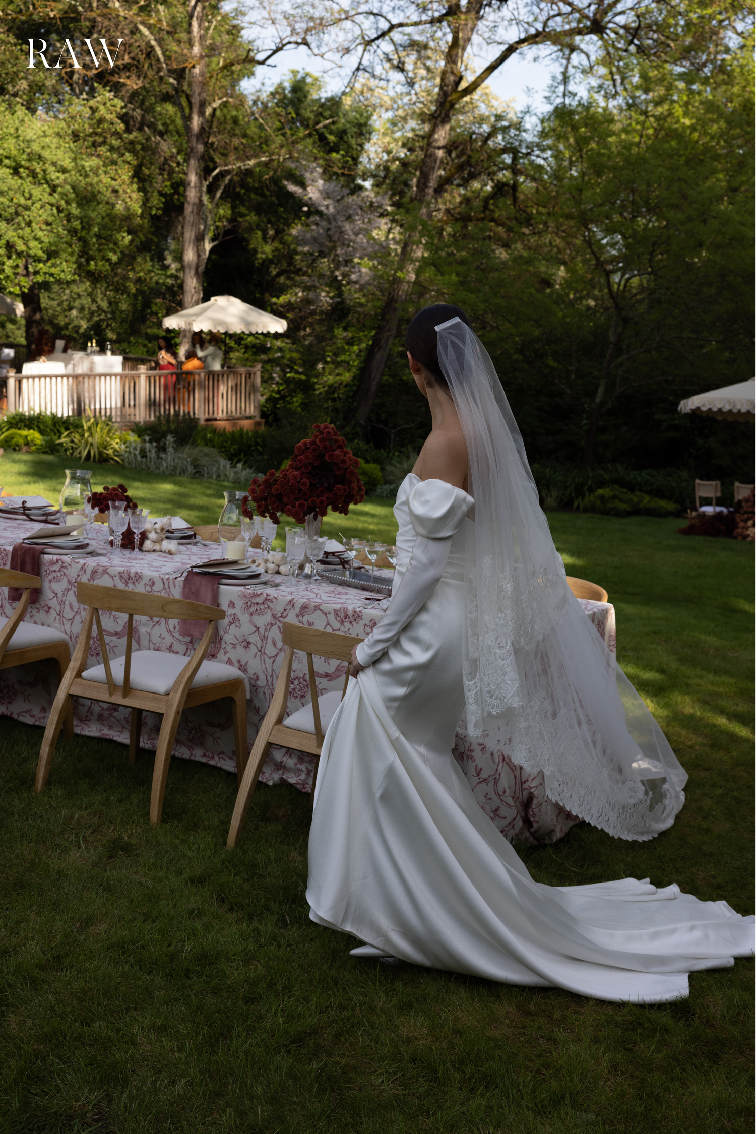 Bride in sleek white gown stands by decorated outdoor wedding table.