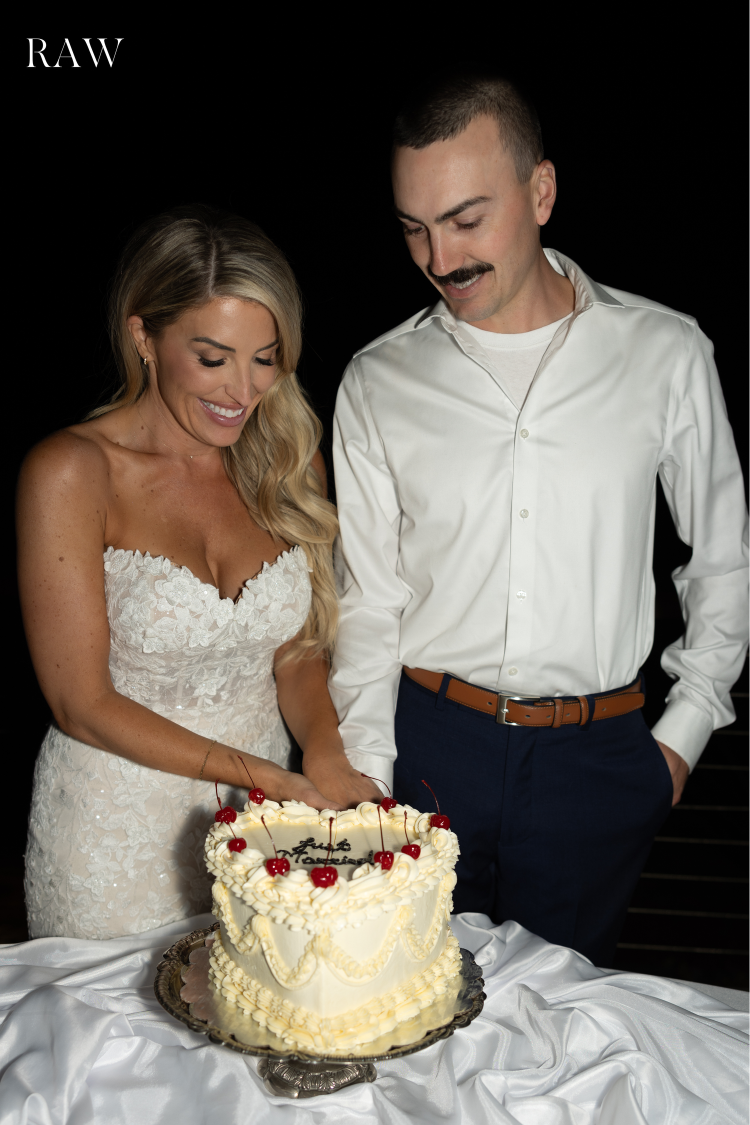 Couple in wedding attire sharing a moment while cutting their white frosted cake.