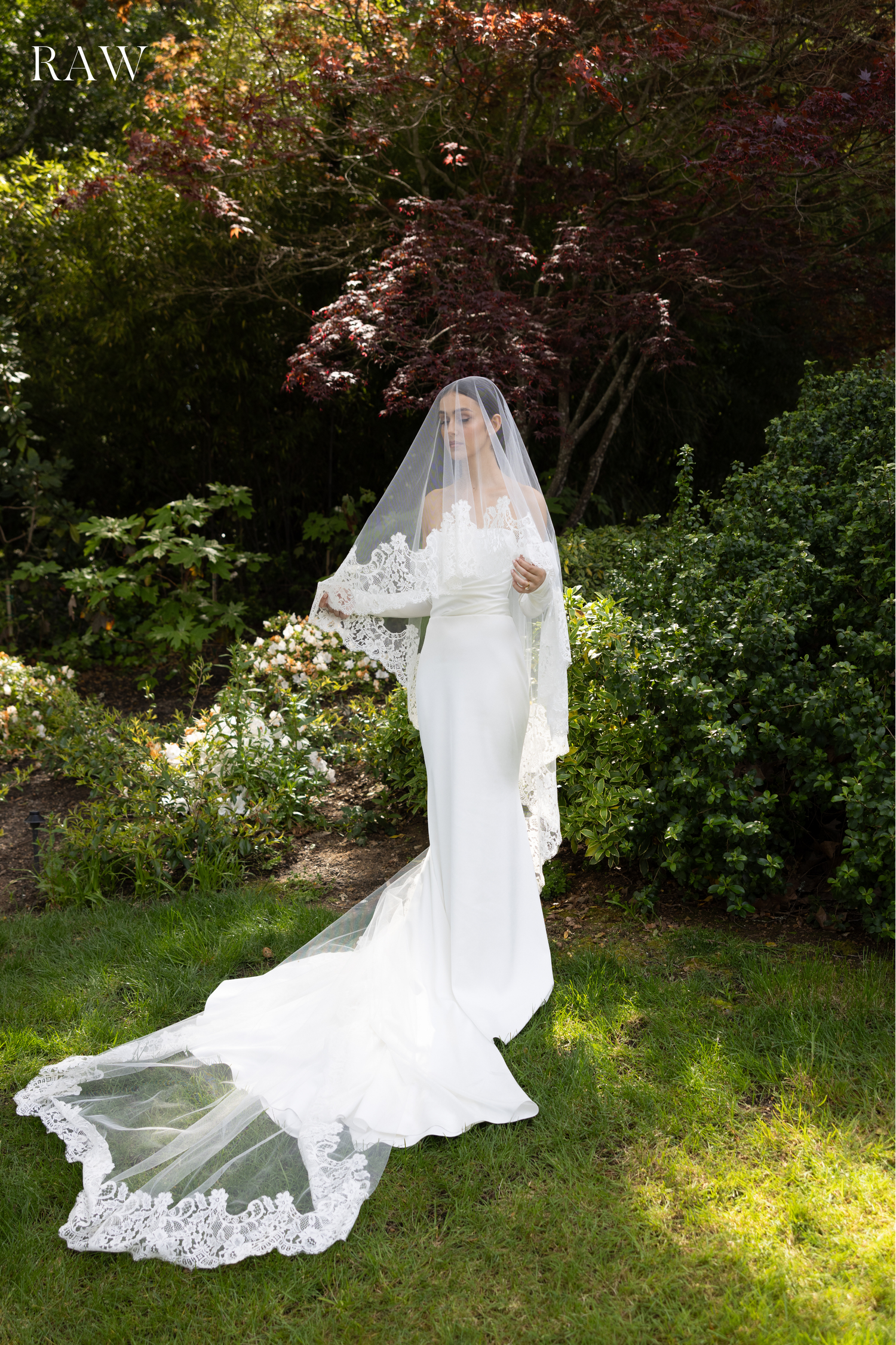 Elegant white wedding dress with flowing lace train photographed in a garden setting with natural lighting.