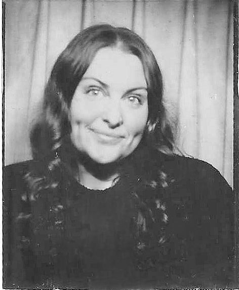 A black and white portrait showing Danielle Conner - California wedding photographer with a warm smile against a light curtain background.