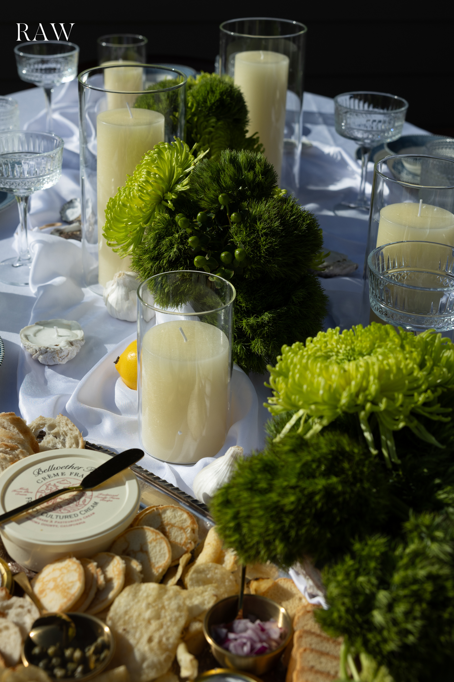 Elegant table setting with green floral arrangements, white candles, and appetizer plates.