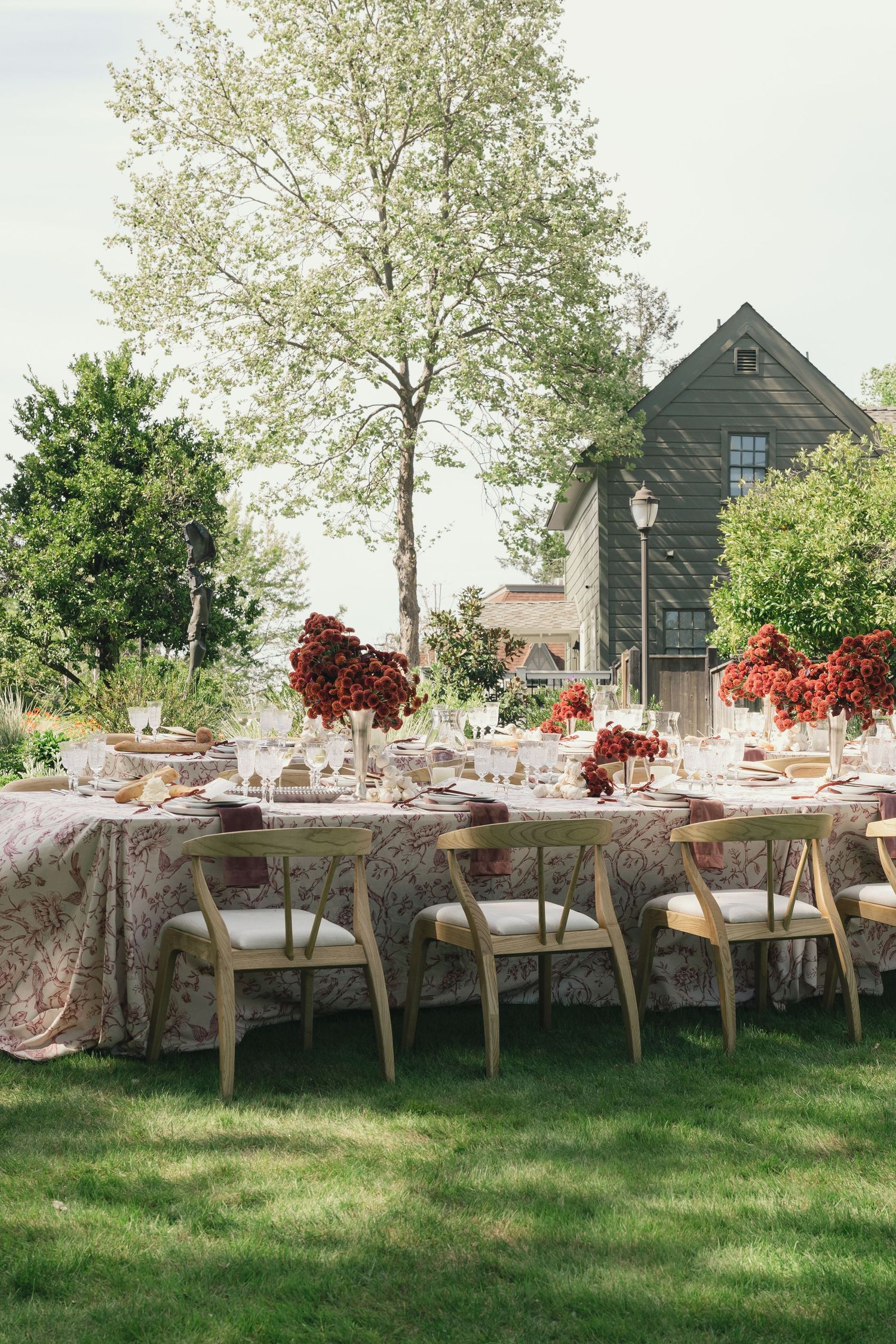 Outdoor wedding reception tables set under trees with elegant place settings and floral centerpieces.