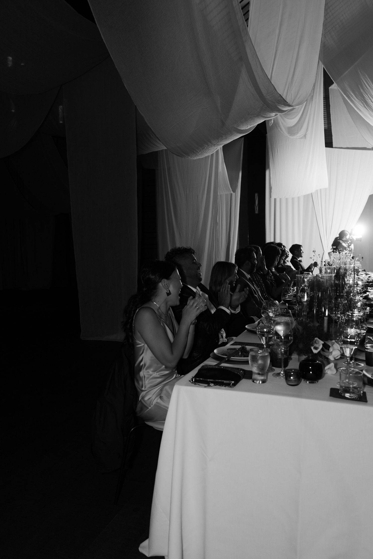 Dimly lit wedding reception table with guests enjoying dinner and conversation.