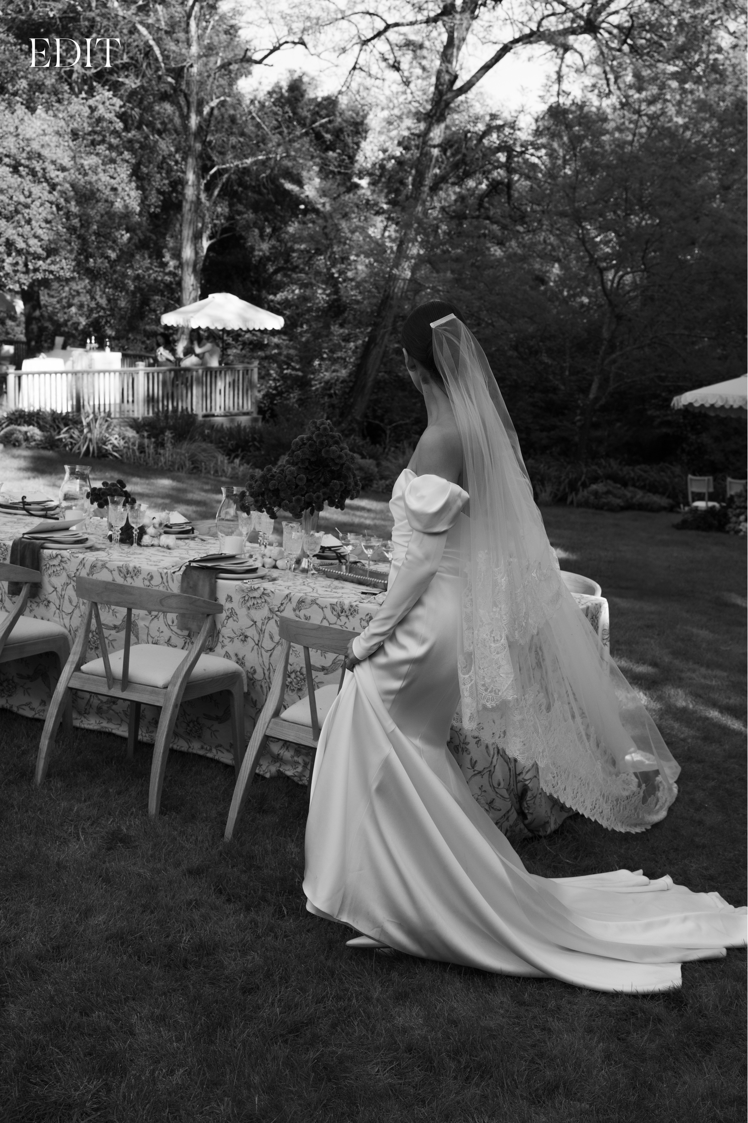 Black and white photo of bride in elegant gown near outdoor reception table setting.
