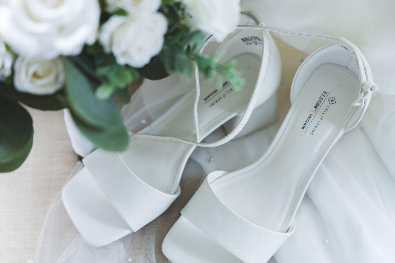 White bridal shoes with delicate floral decorations and pearls arranged with wedding accessories.