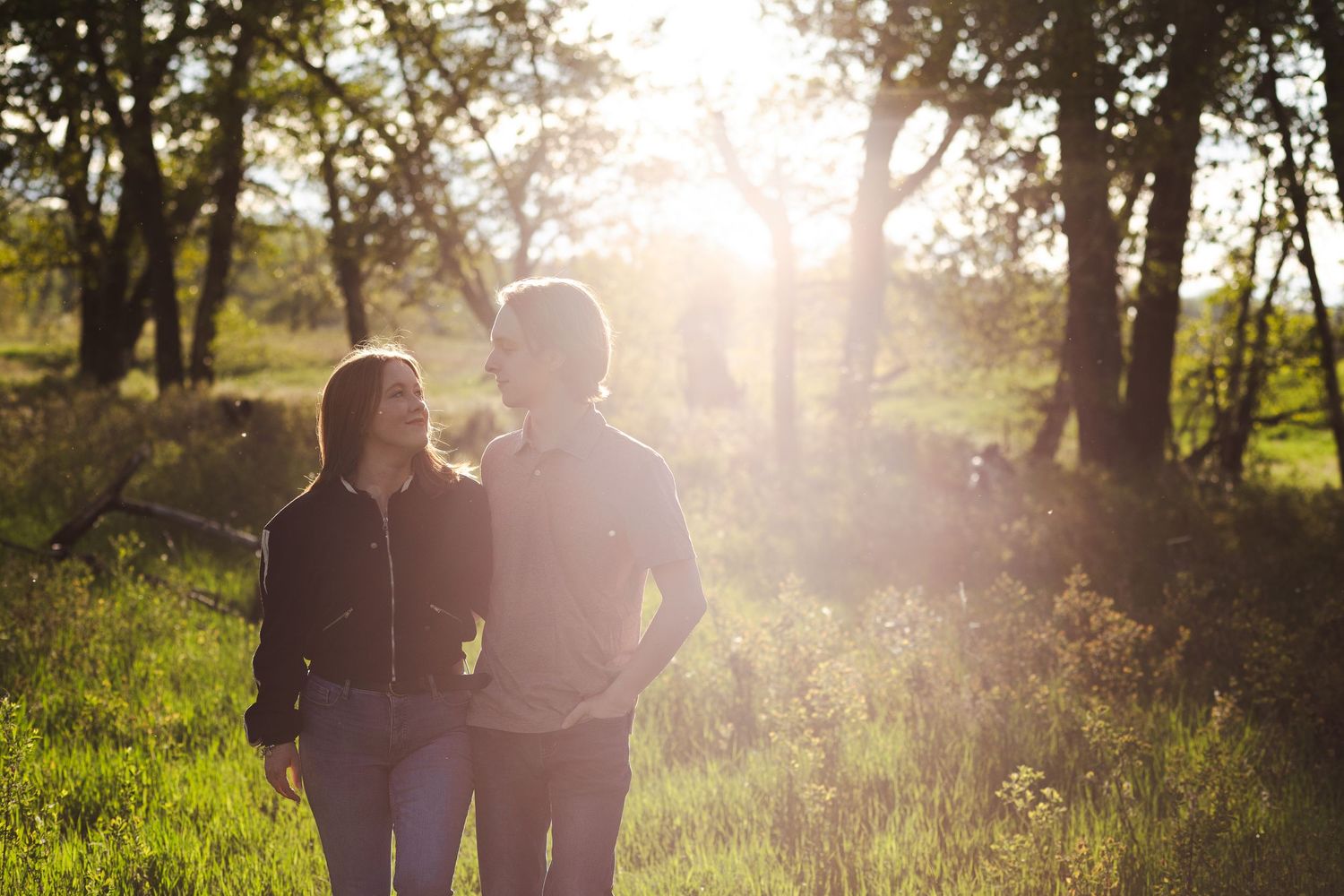 Couple walking through a wooded area backlit by golden sunlight.