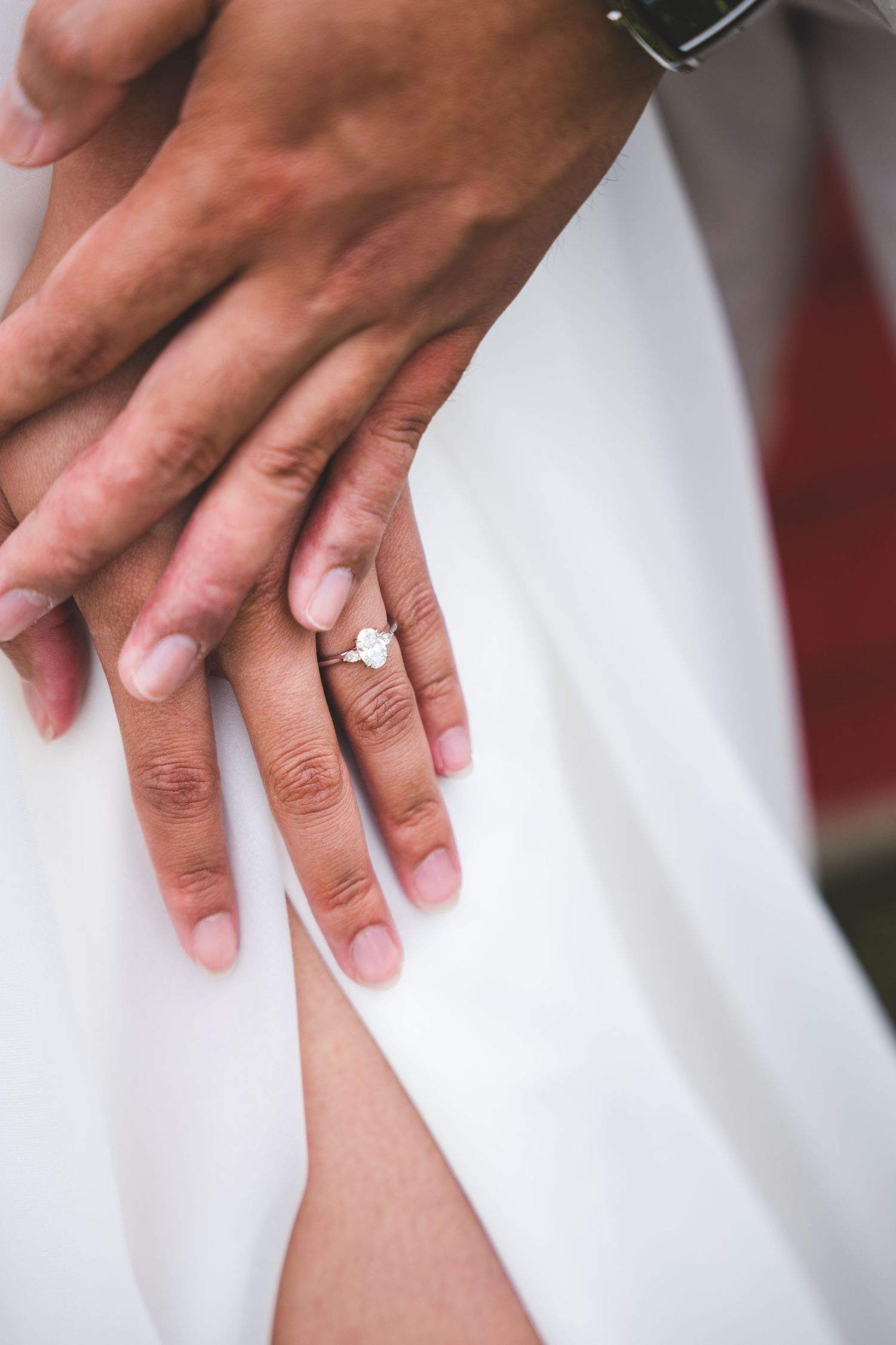 Close-up of hands with French manicured nails against a white wedding dress background.
