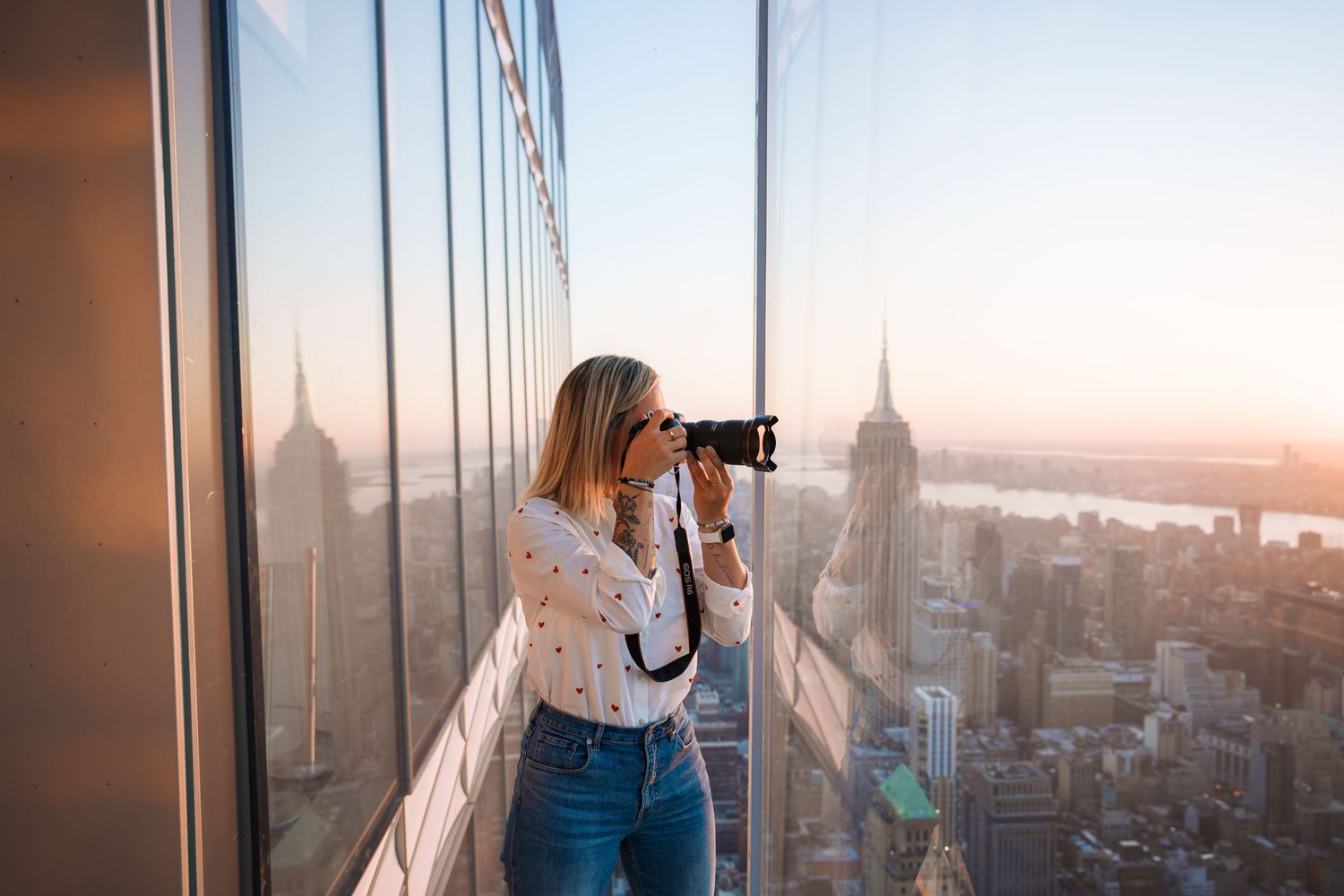 Adélaïde Chantilly taking a photo from a high-rise building in NYC, with a glowing sunset casting warm light across the skyline.