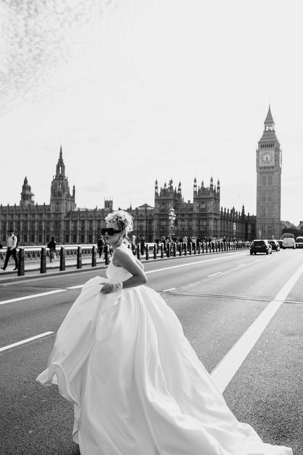 A bride in a flowing white ballgown poses on Westminster Bridge with Big Ben and Parliament in the background in London.
