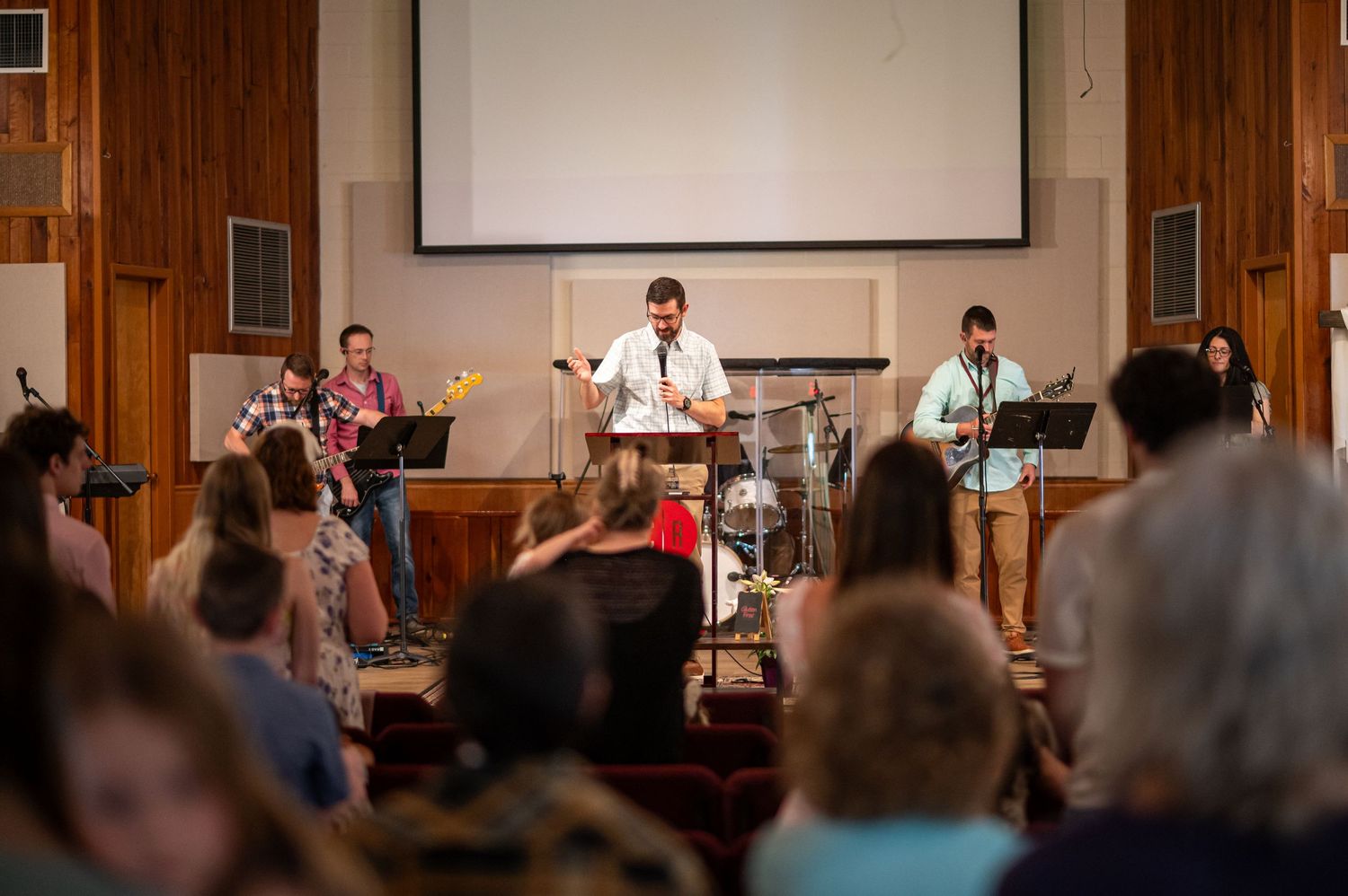 a Crossroads church member stands on stage behind a pulpit during Sunday morning service, with church members visible in the foreground