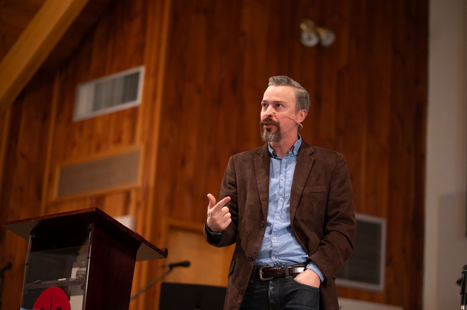 Pastor Chris stands on the stage at Crossroads Morgantown during Sunday morning church service, preaching from an open Bible on a pulpit