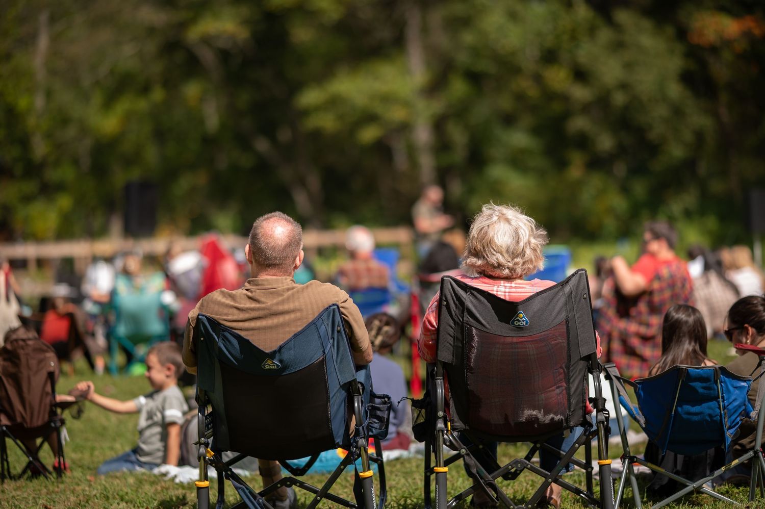 view from behind a crowd of church attendees sitting outside in camp chairs, listening to a Crossroads pastor preaching in the distance