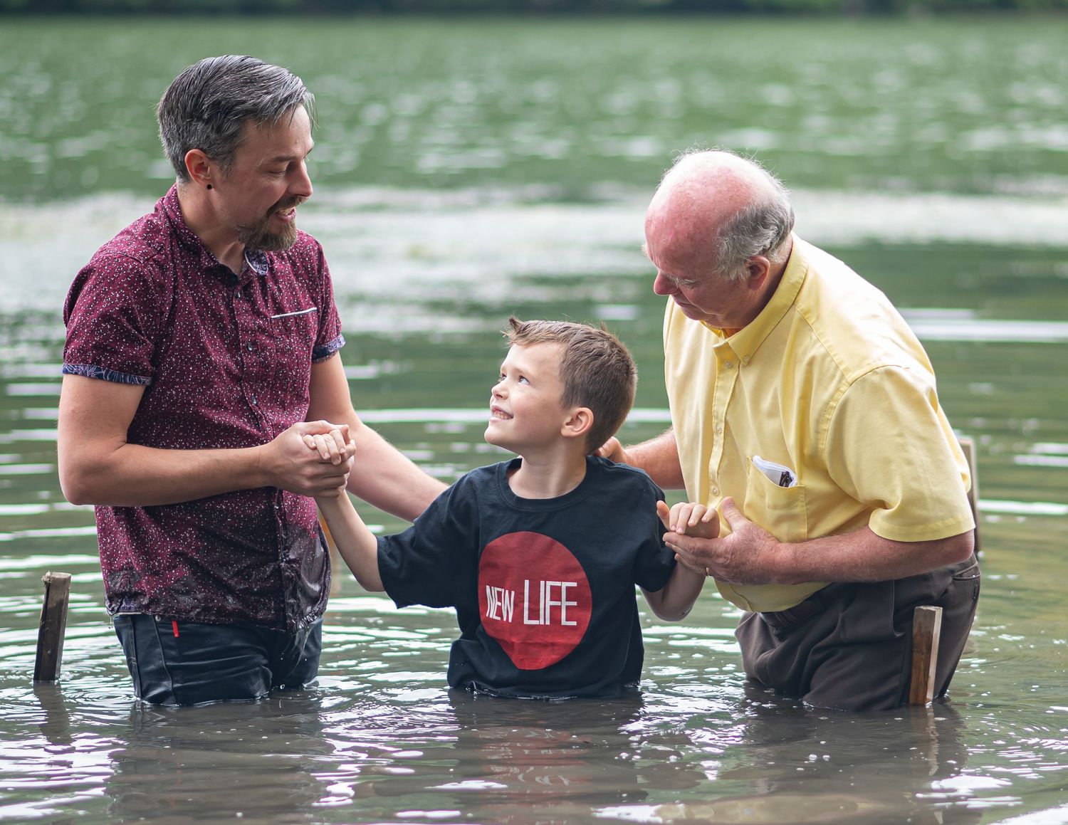 Pastor Chris stands in the river with his son and his father at a baptism at an outdoor Sunday morning church service in Morgantown, WV