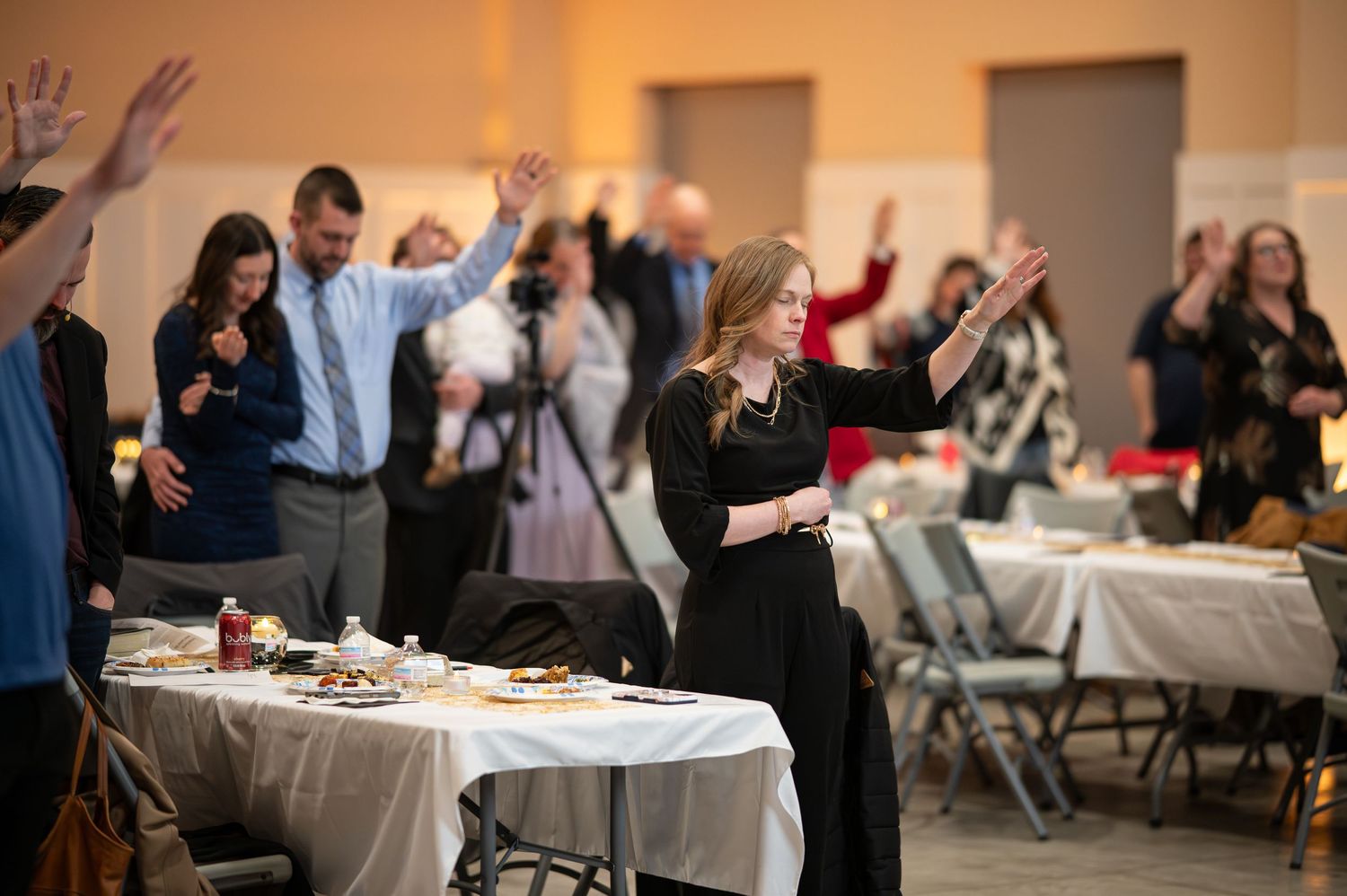 a group of Crossroads members stand together with hands raised, praying with eyes closed