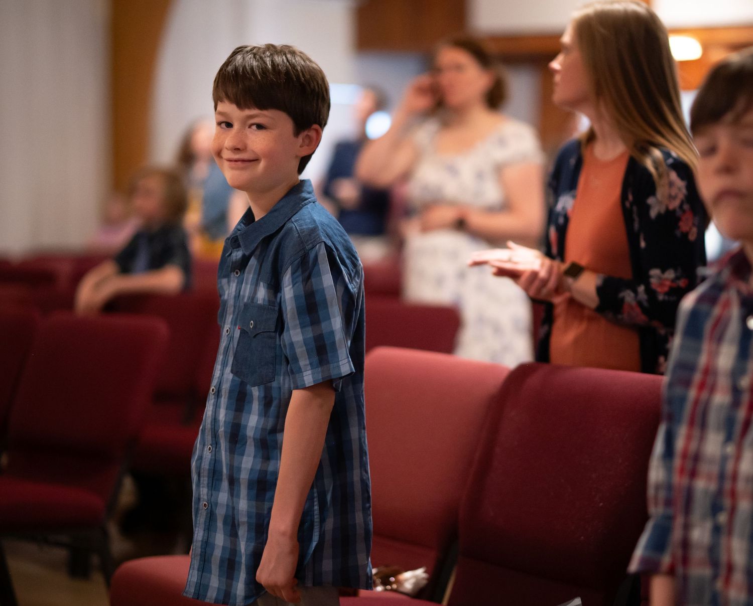 a young boy attending Sunday morning service at Crossroads church smiles at the camera, with other church members visible in the background