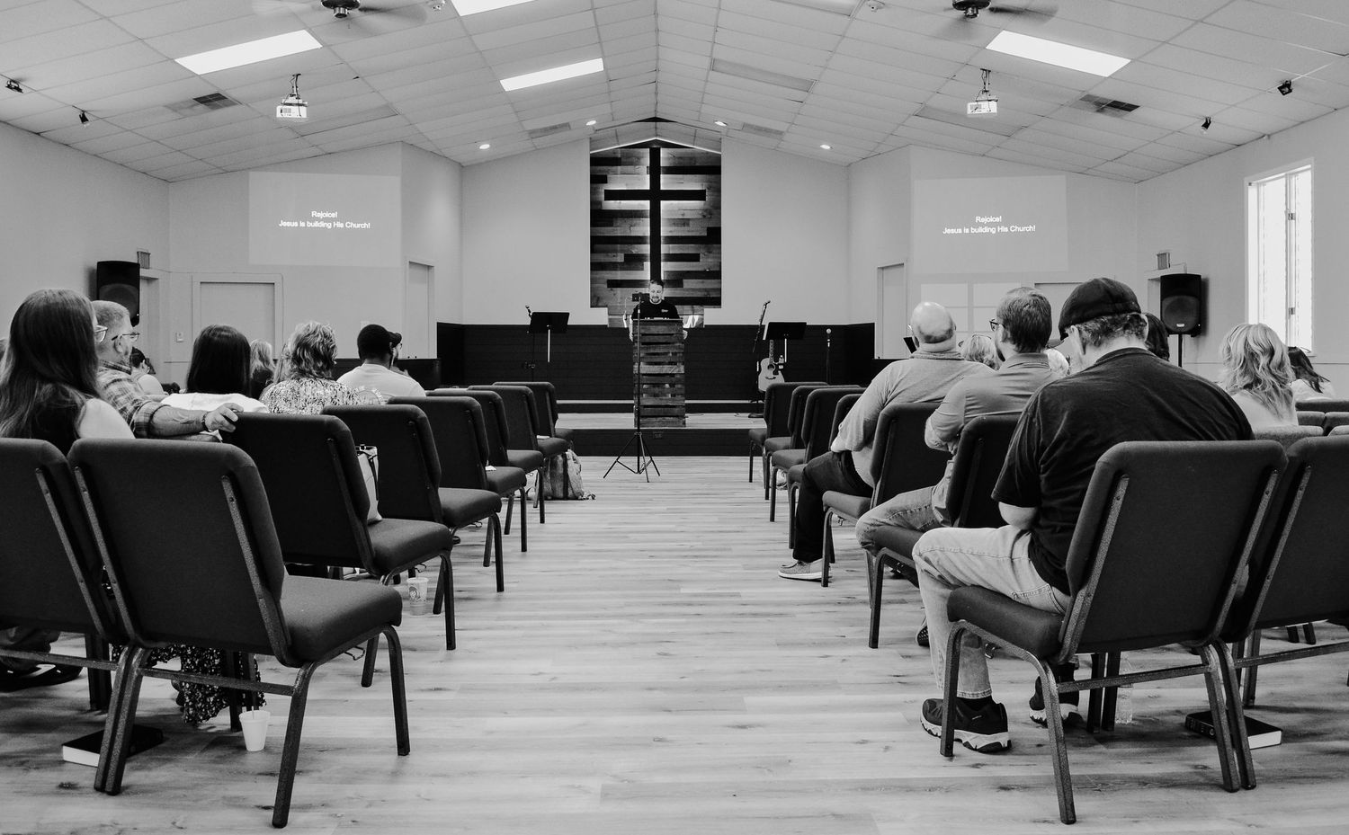 a view down the center aisle of Crossroads Fairmont, with members seated in chairs on either side, during a Sunday morning church service