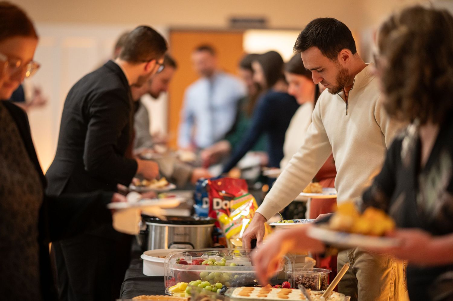 Crossroads members file down both sides of a potluck table loaded with food, filling plates for a meal