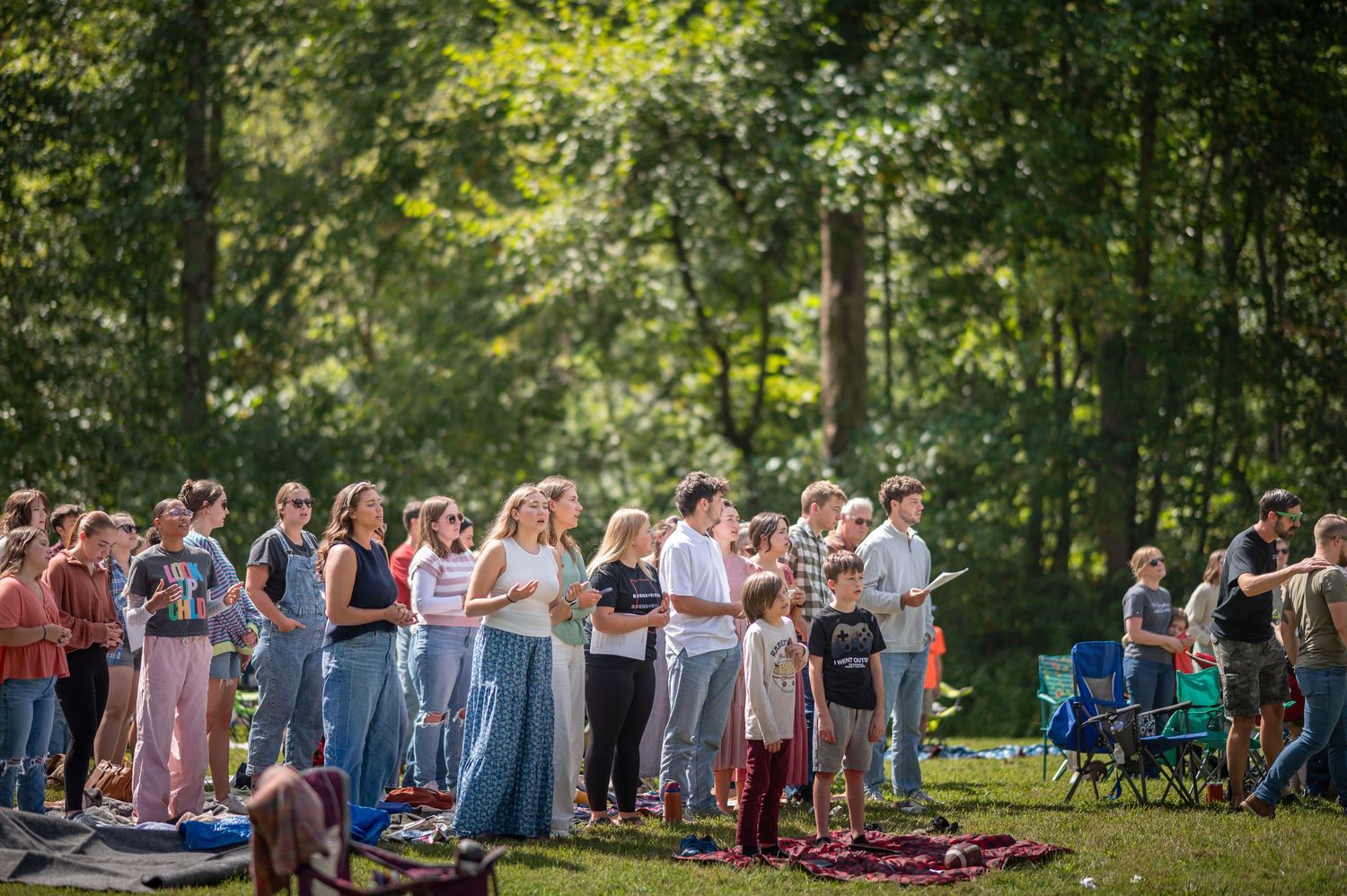 a crowd of Crossroads church attendees stand and sing outdoors in a large field during an outdoor Sunday service in Morgantown