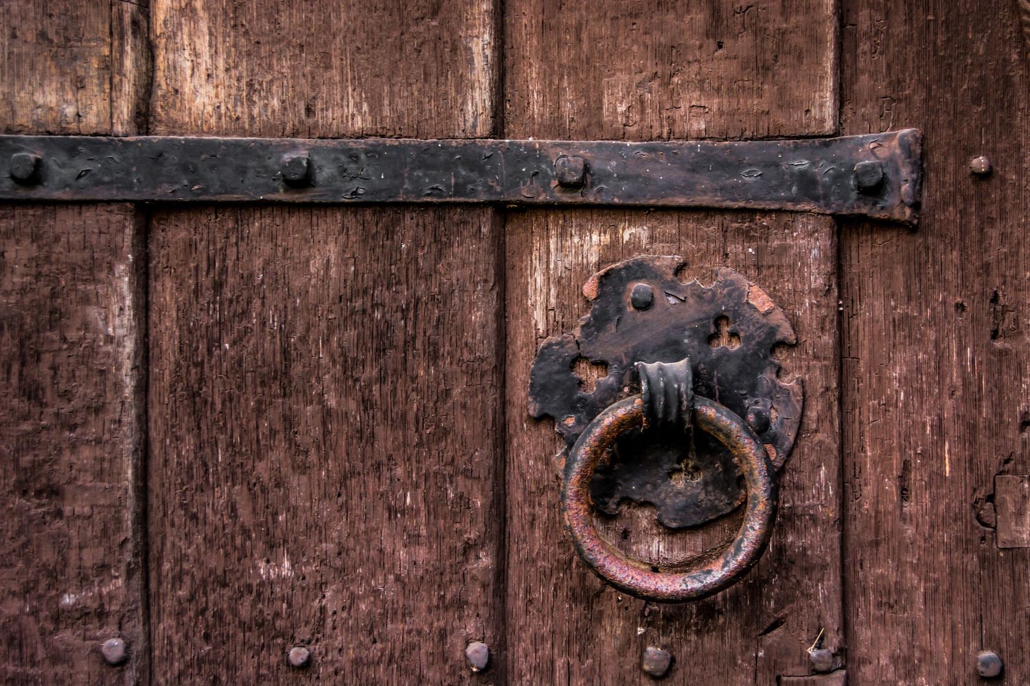 closeup image of a very old wooden door with iron hinges and a worn iron handle