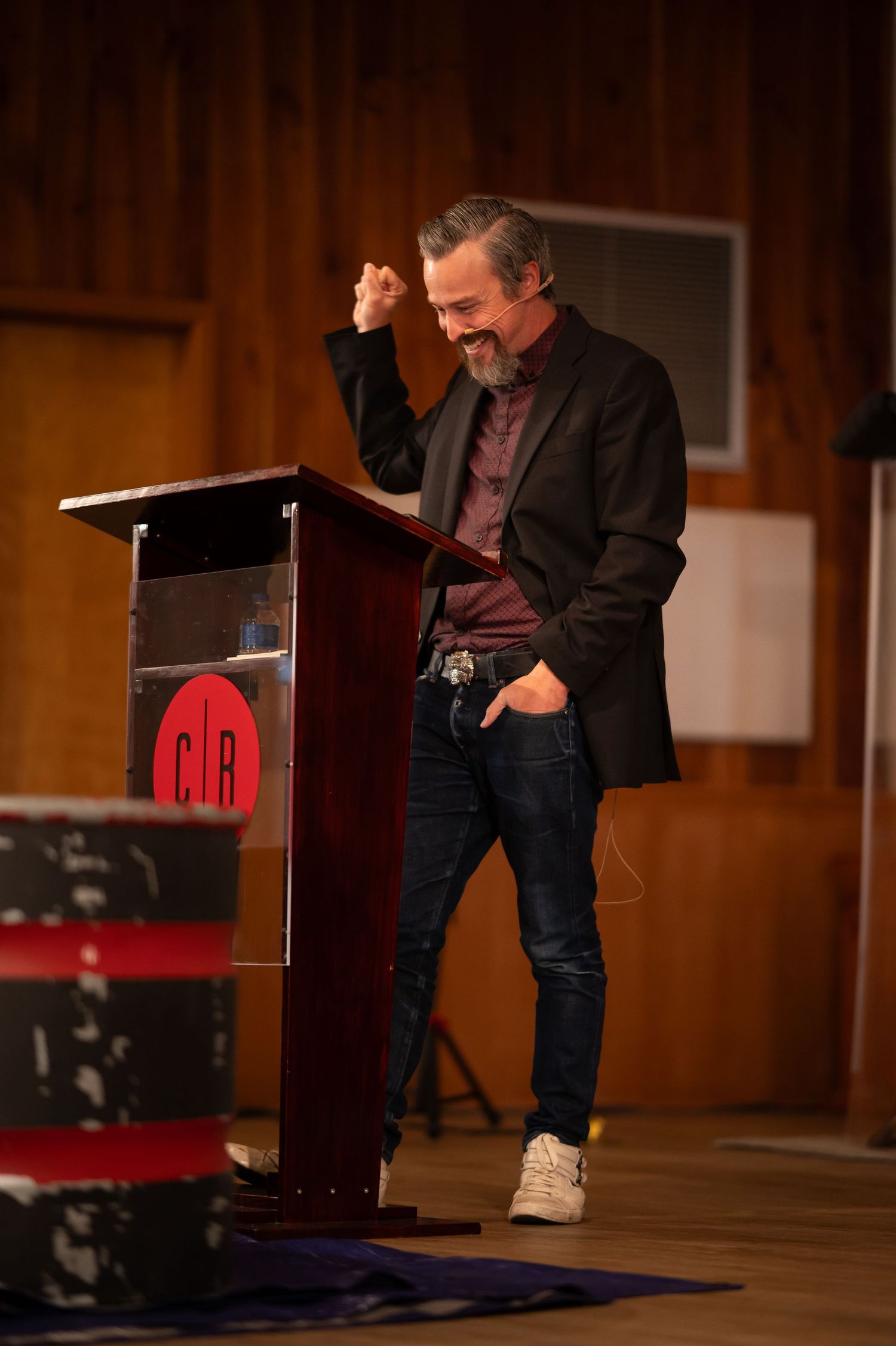 Pastor Chris stands on the stage at Crossroads Morgantown and preaches from the pulpit with one hand raised