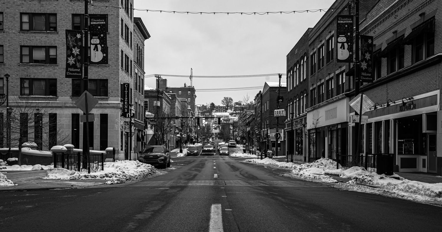 black and white image of High St. in downtown Morgantown in the winter, with cars driving along the street and snow on the sidewalks