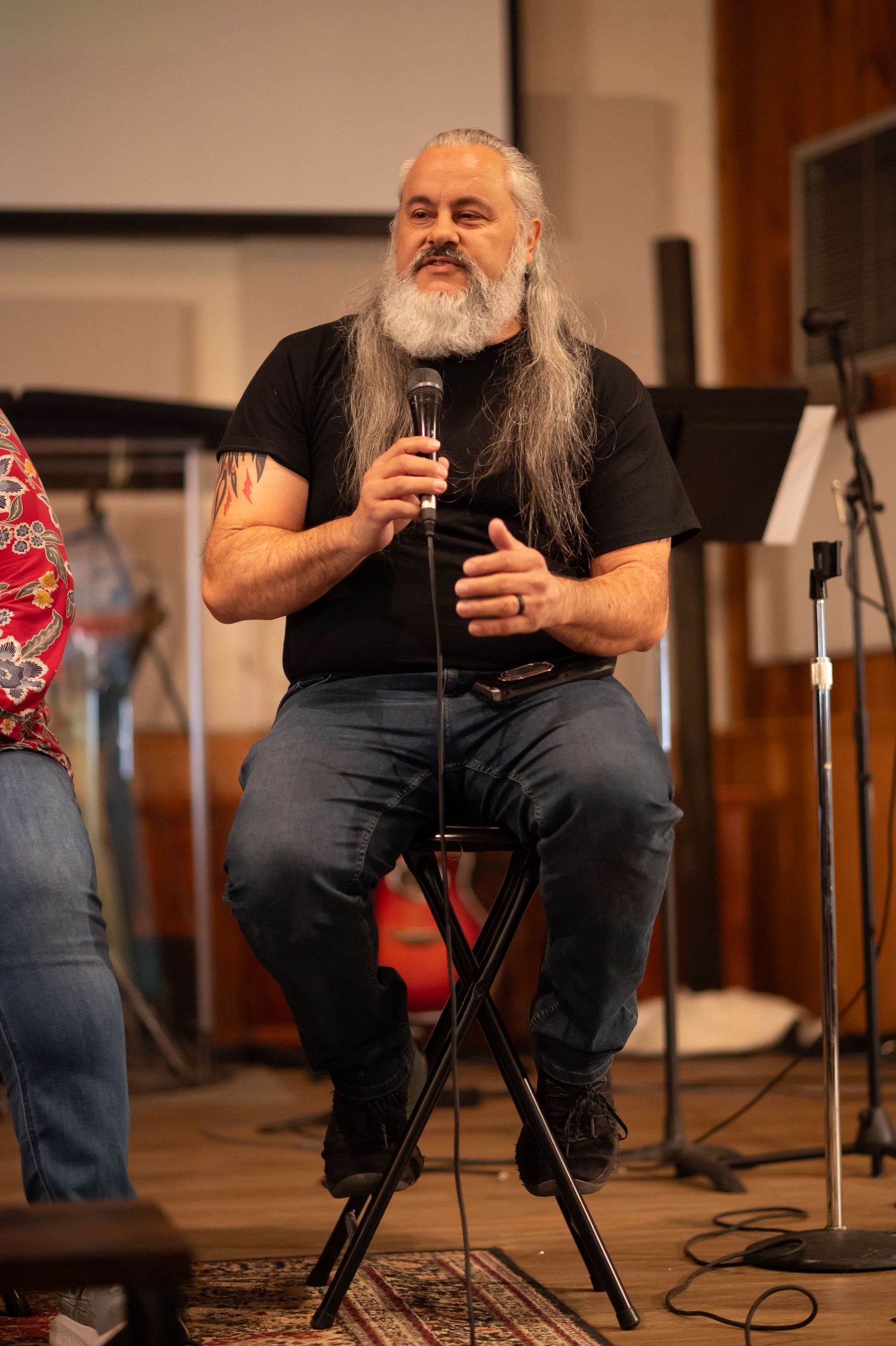 Pastor Chatto speaks into a microphone while sitting on a stool on the stage of Crossroads Morgantown during a Sunday church service
