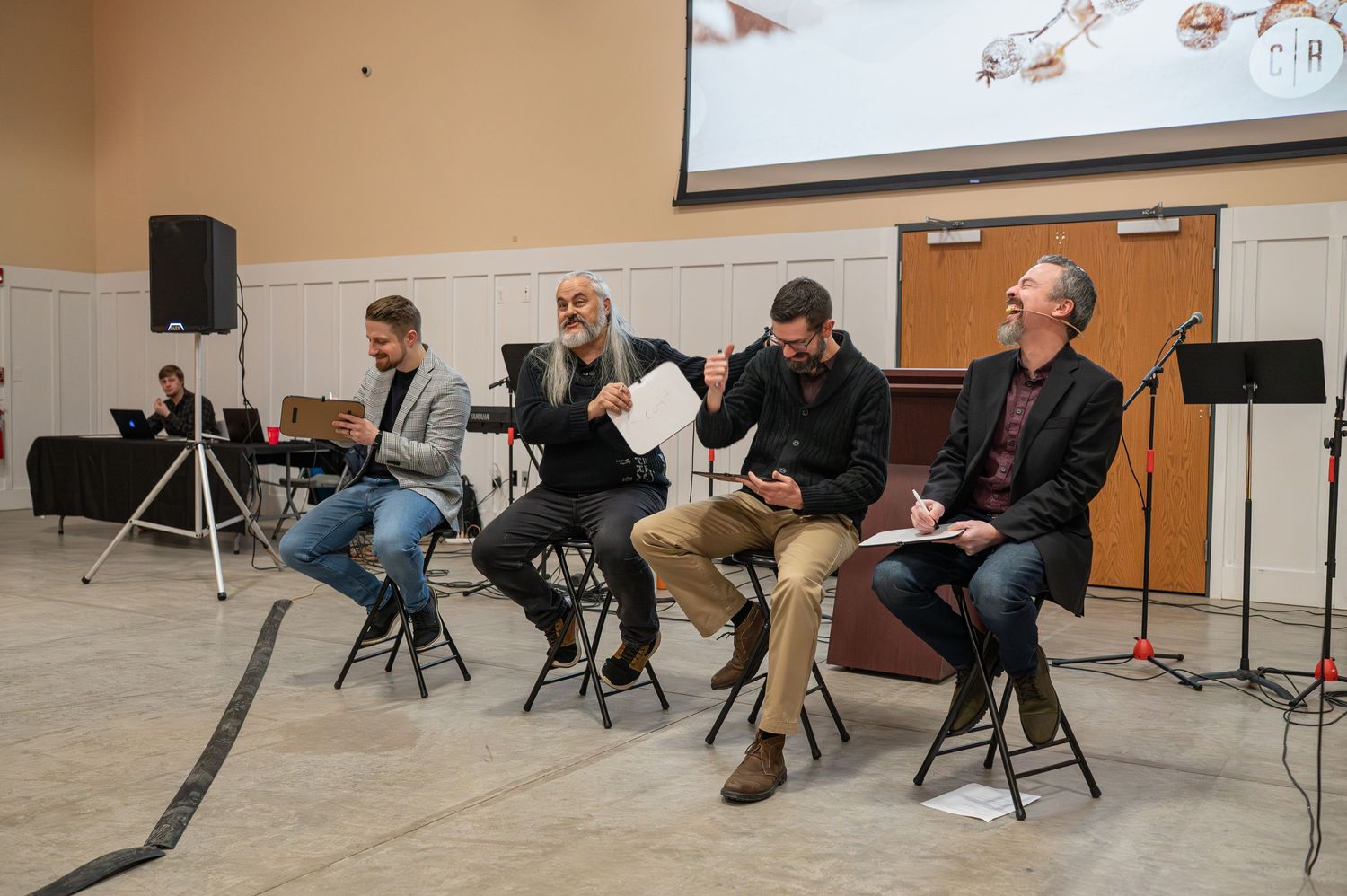 Crossroads pastors sit on stools on stage at an event and laugh together