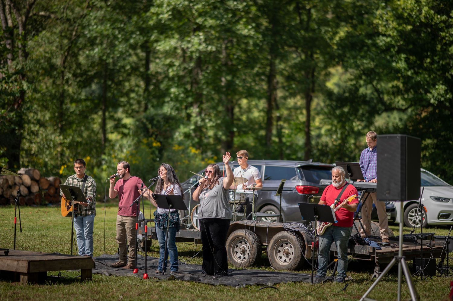 Crossroads worship team leads worship with instruments and microphones from a mobile stage in a large green field at an event