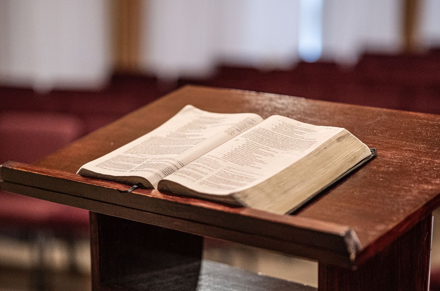 an open ESV Bible with well-worn pages lies open on a wood pulpit in the auditorium of Crossroads Morgantown with seats in the background